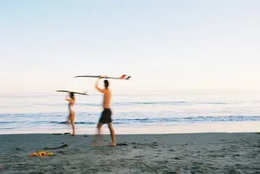 A man and a woman are holding surfboards on the beach.