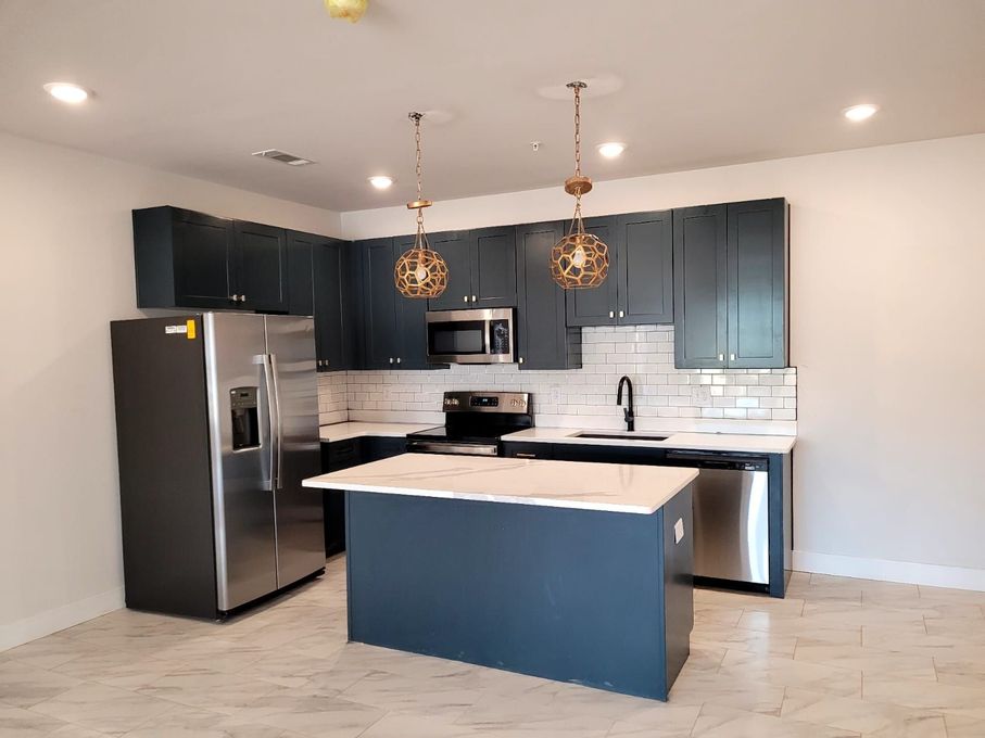 A kitchen with blue cabinets , stainless steel appliances , and a large island.