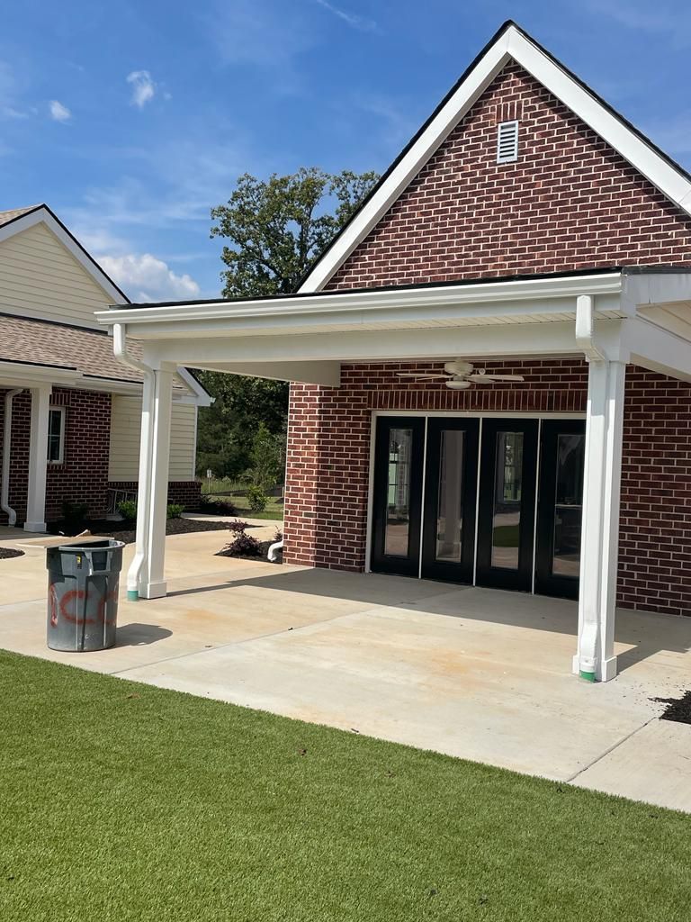 A brick building with a white porch and a trash can in front of it.