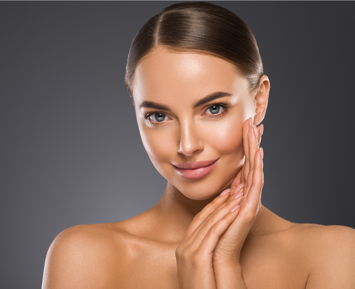 Frau mit gebräunter Haut, lächelnd und ihr Gesicht berührend, vor dunklem Hintergrund.