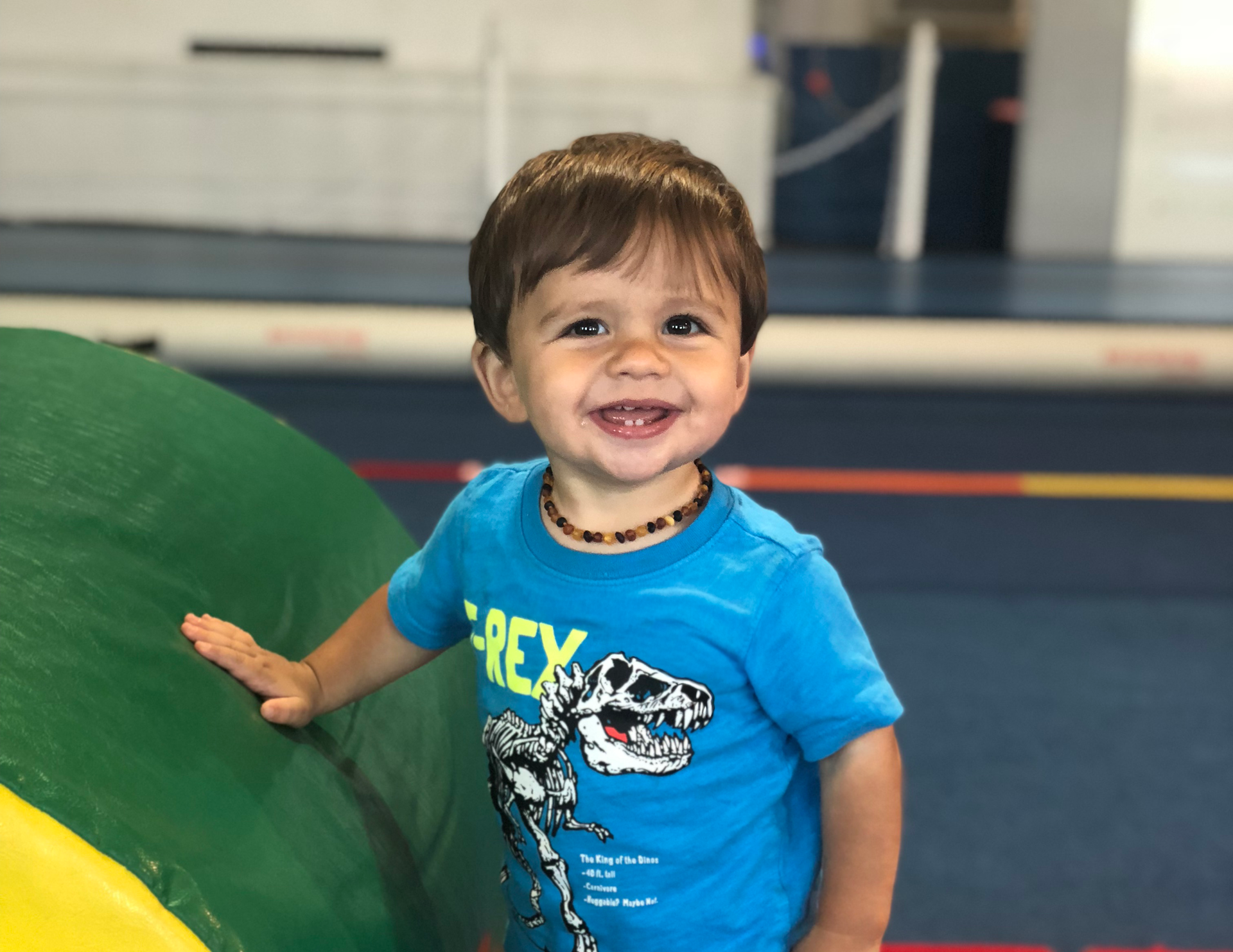 Smiling baby grasping wooden gymnastic rings, wearing a blue and white striped tank top.