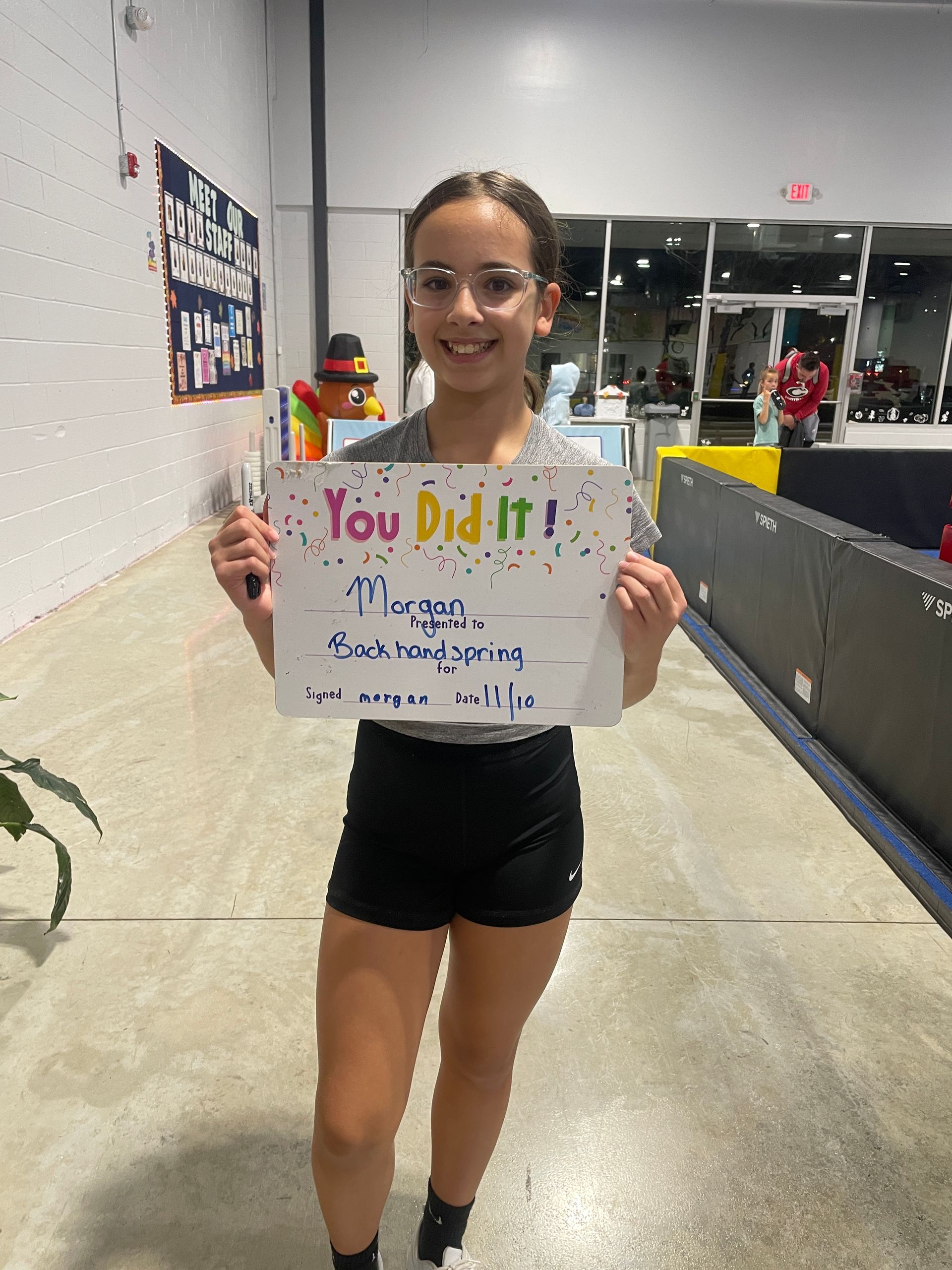 Young gymnast in red leotard doing splits on a balance beam.