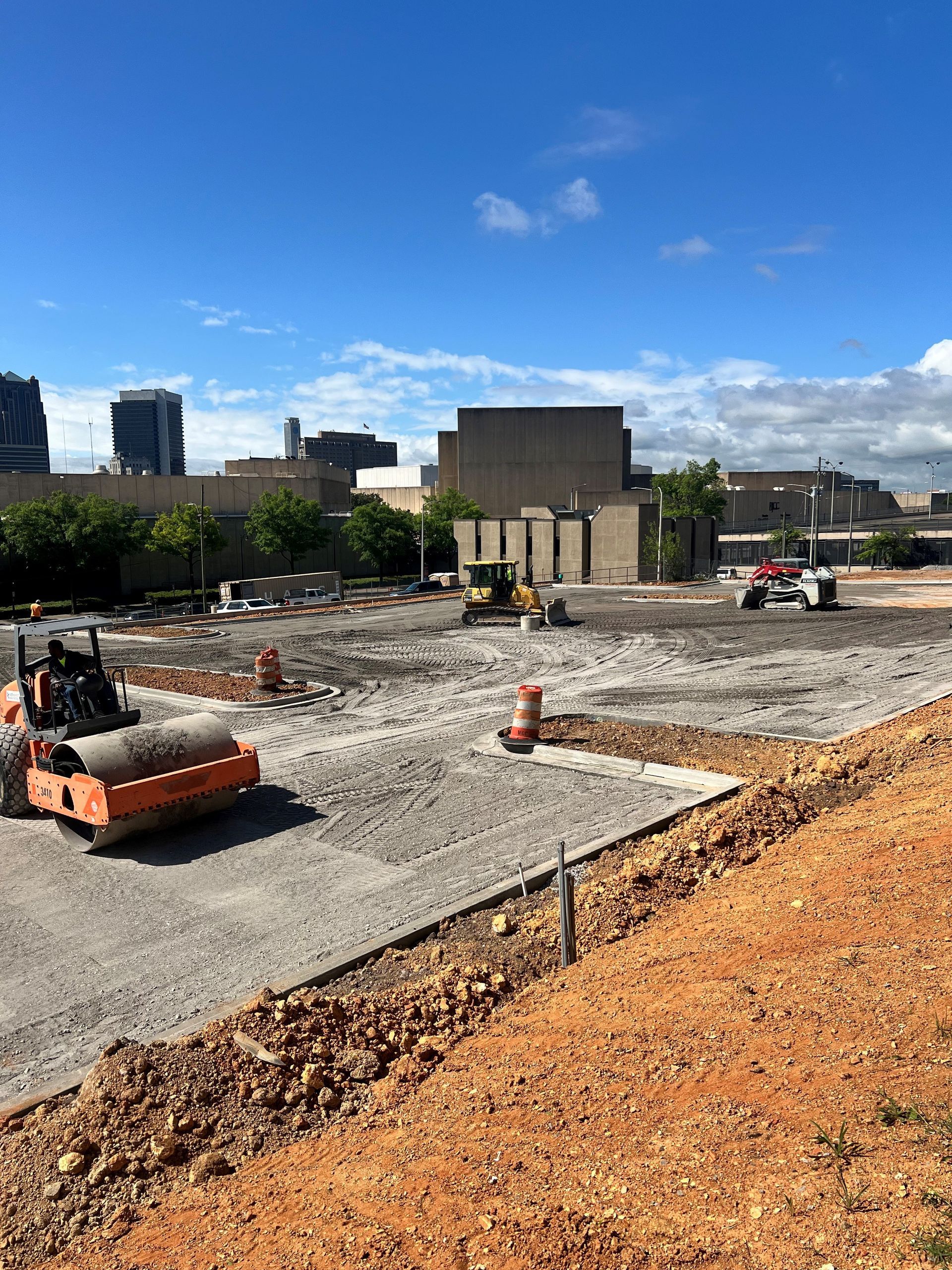 A construction site with a large building in the background and a roller in the foreground.