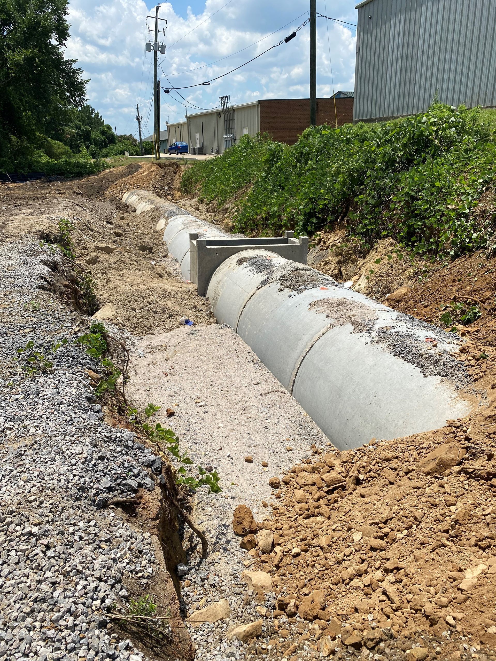 A large concrete pipe is sitting in the dirt next to a gravel road.