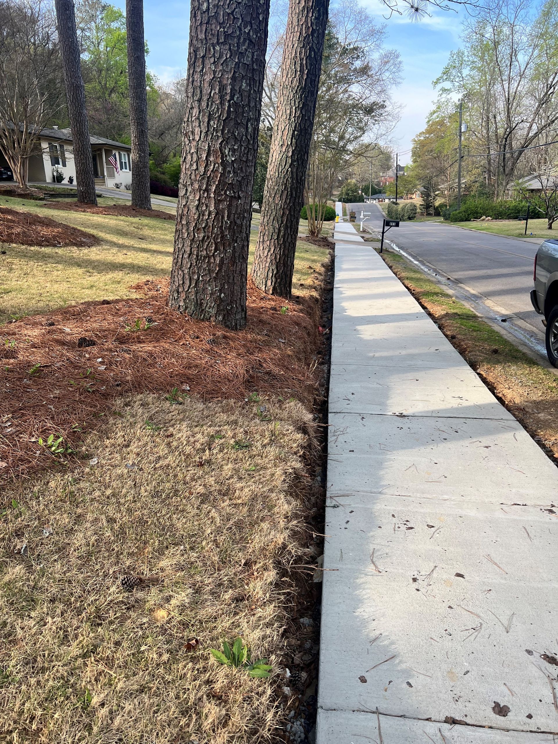A sidewalk with trees on the side of it and a truck parked on the side of the road.