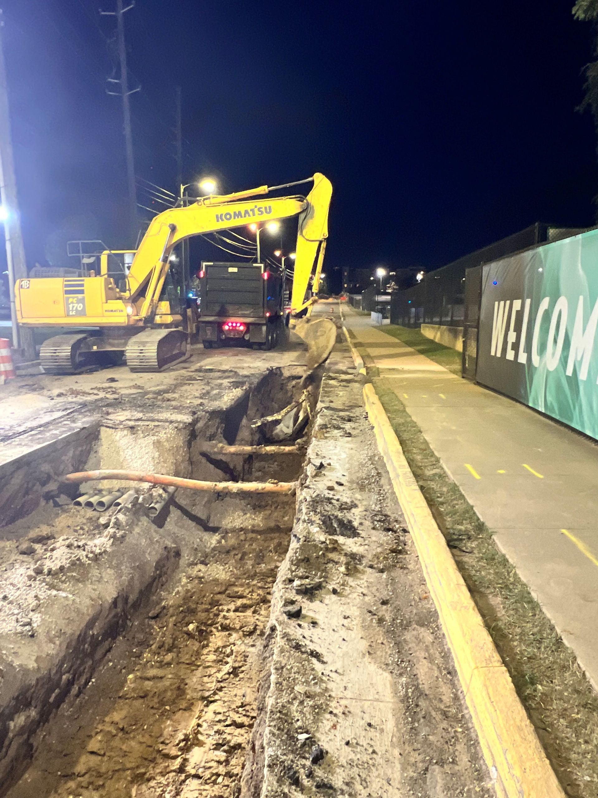 A yellow excavator is digging a hole in the ground at night.