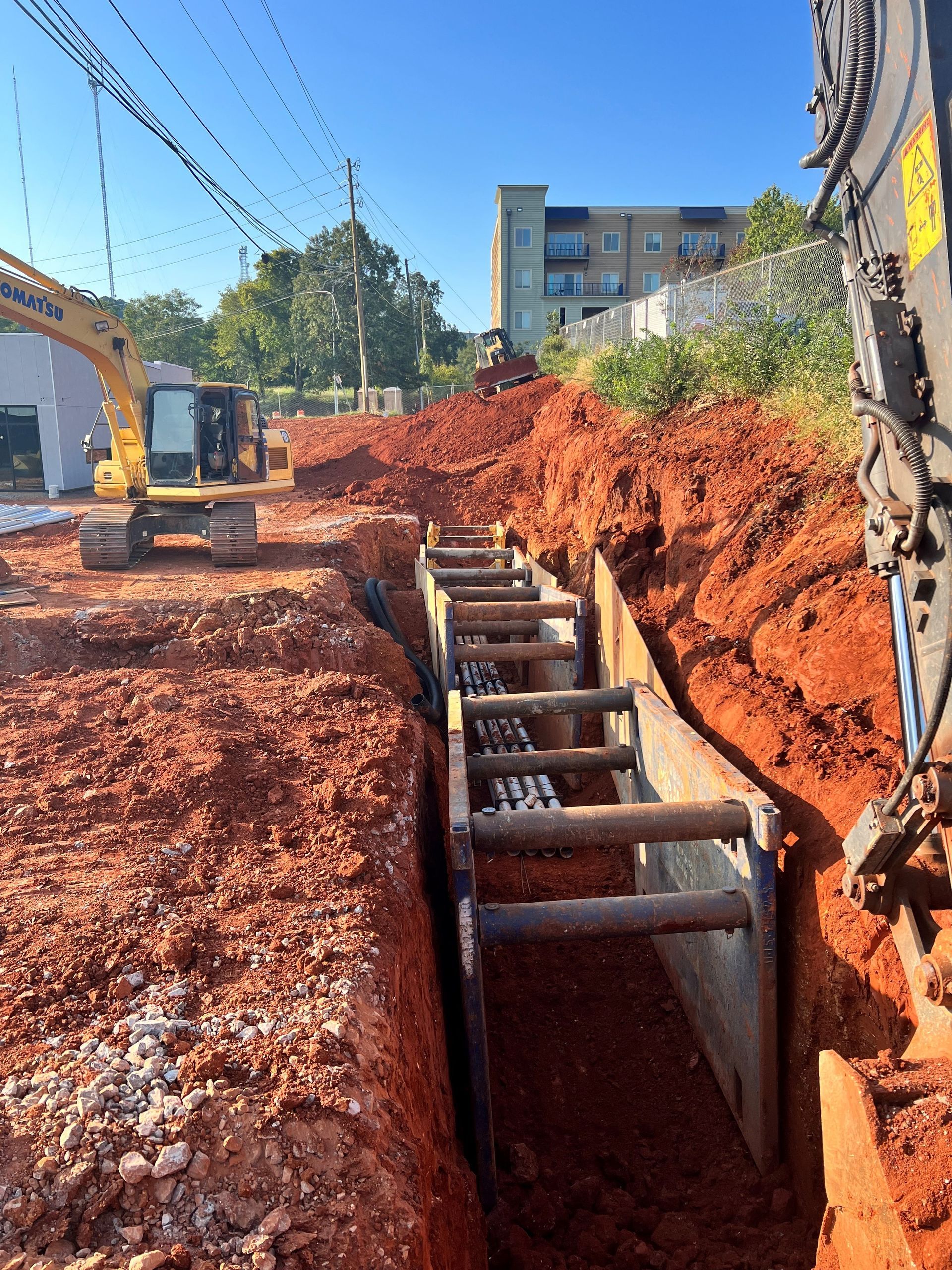 A construction site with a yellow excavator and a ladder in the dirt.
