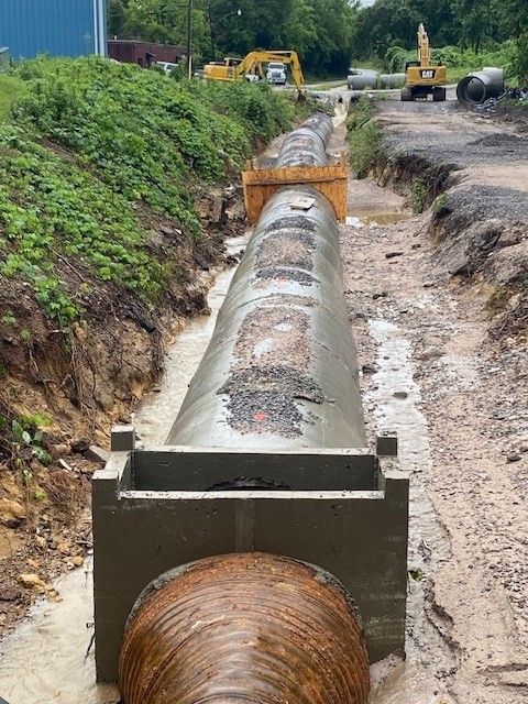 A large concrete pipe is being installed in a trench.