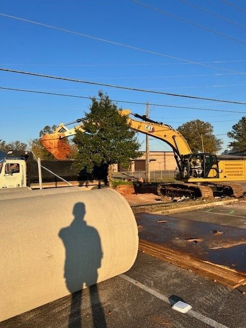 A shadow of a man is cast on a concrete pipe in a parking lot.