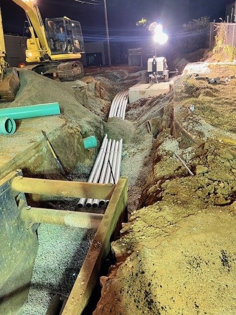 A construction site with a yellow excavator and a bunch of pipes