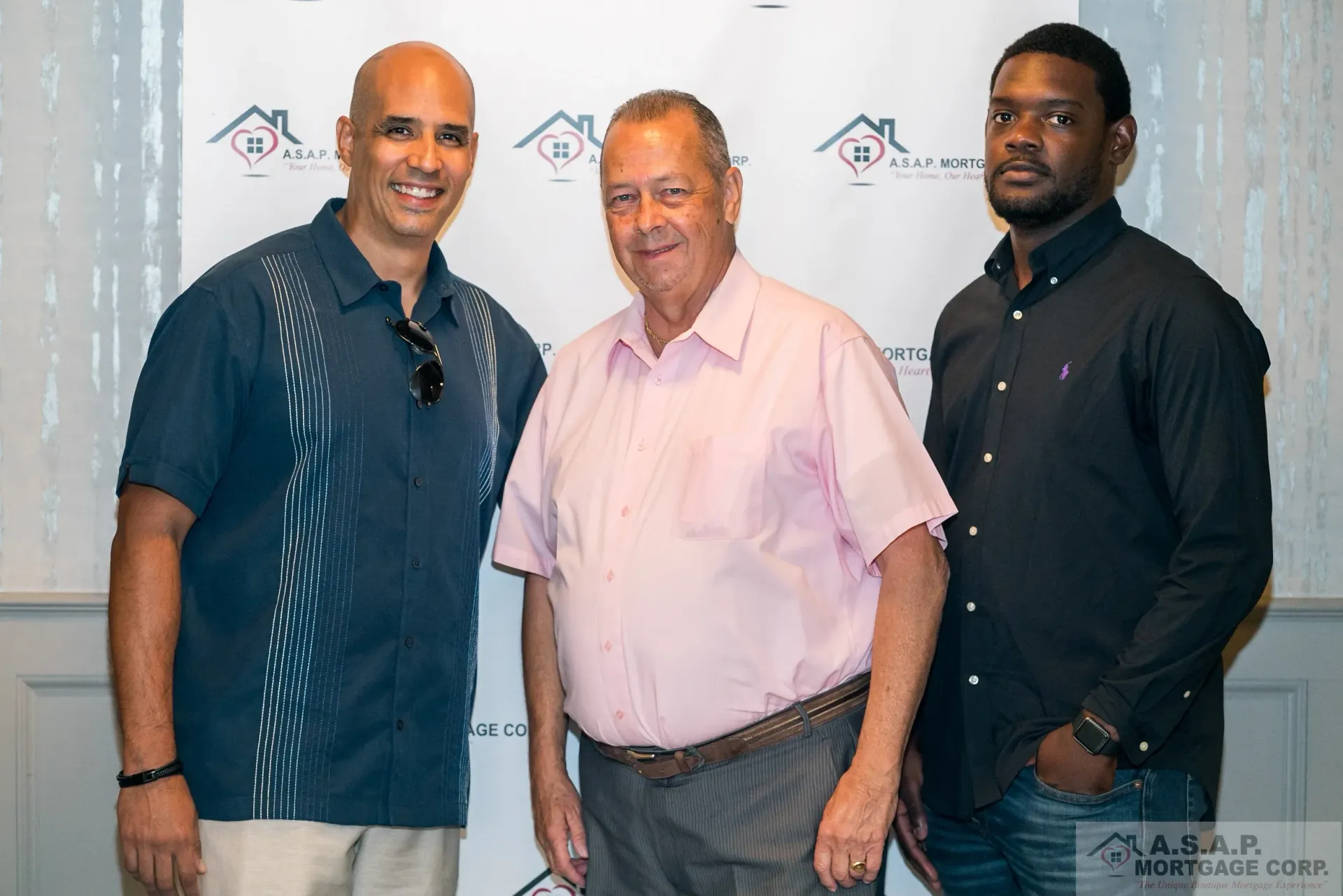Three men are posing for a picture in front of a white wall.