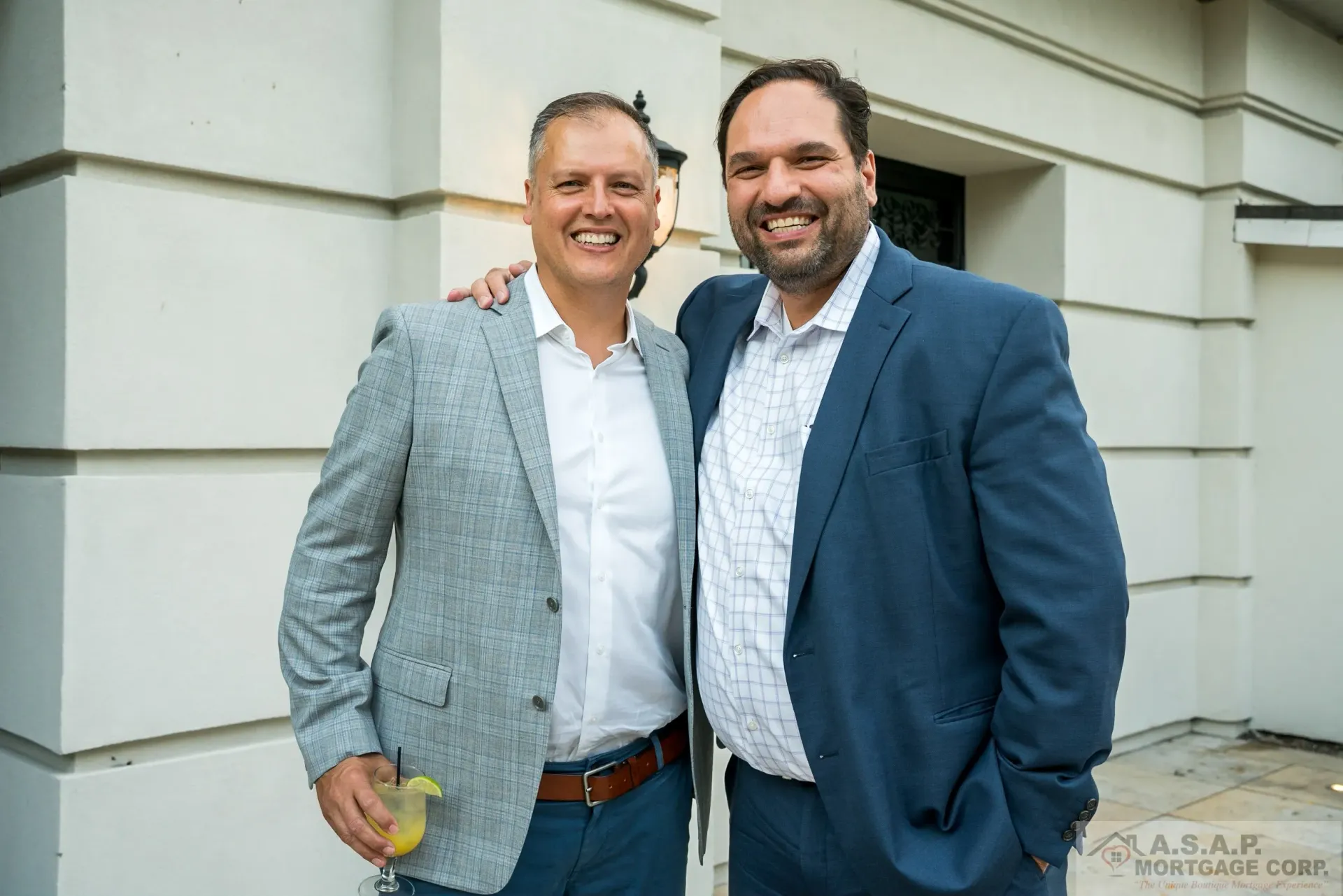 Two men in suits are posing for a picture in front of a building.