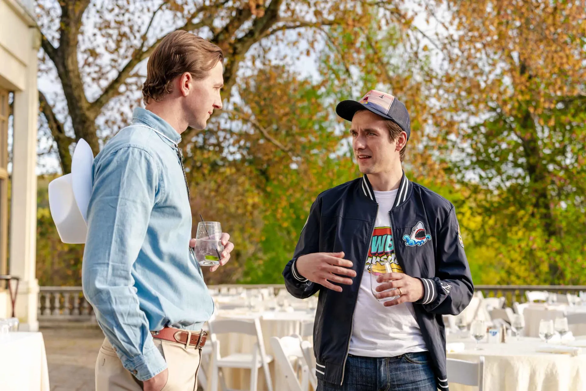 Two men are standing next to each other on a patio talking to each other.