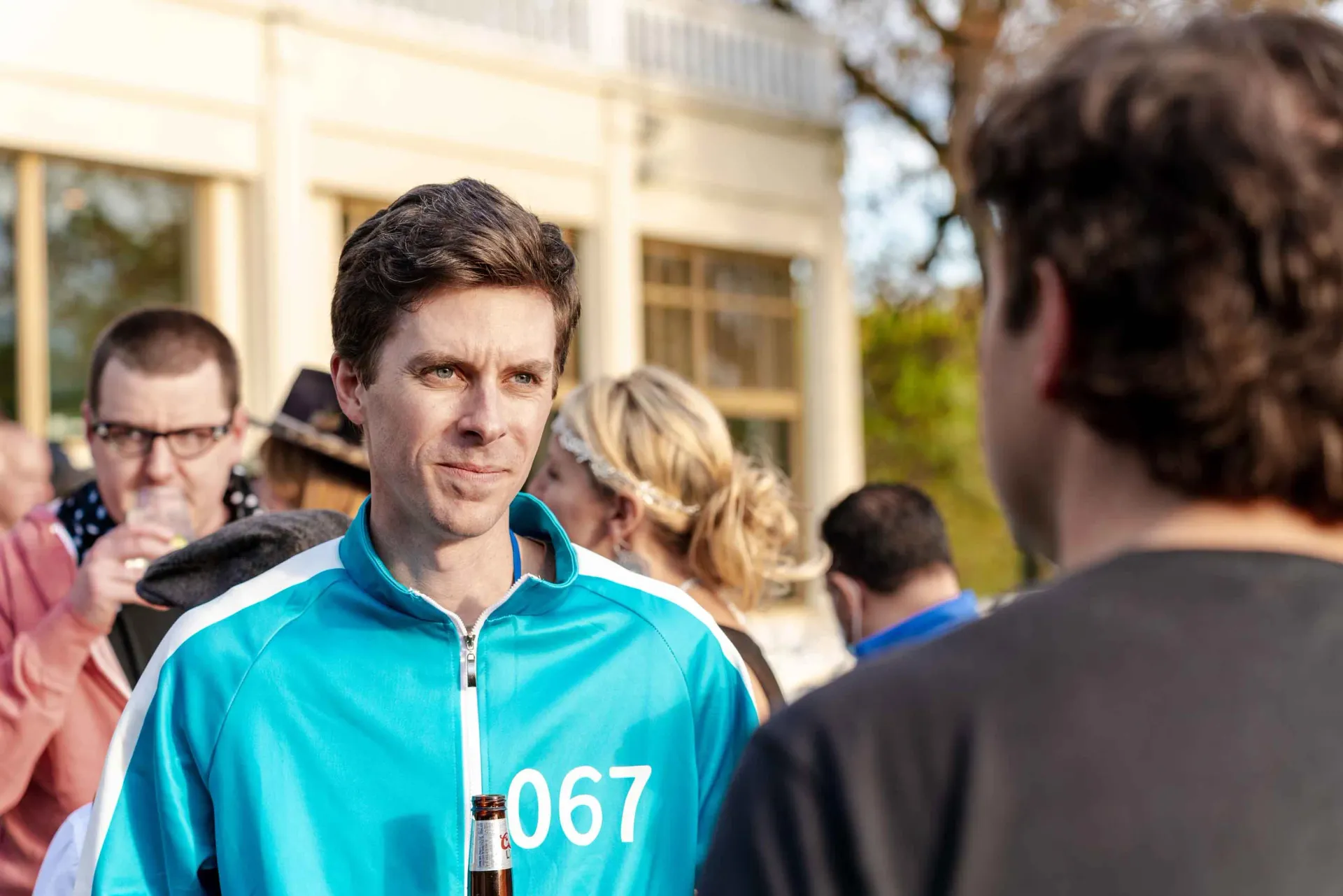 A man in a blue jacket with the number 067 on it is talking to another man.