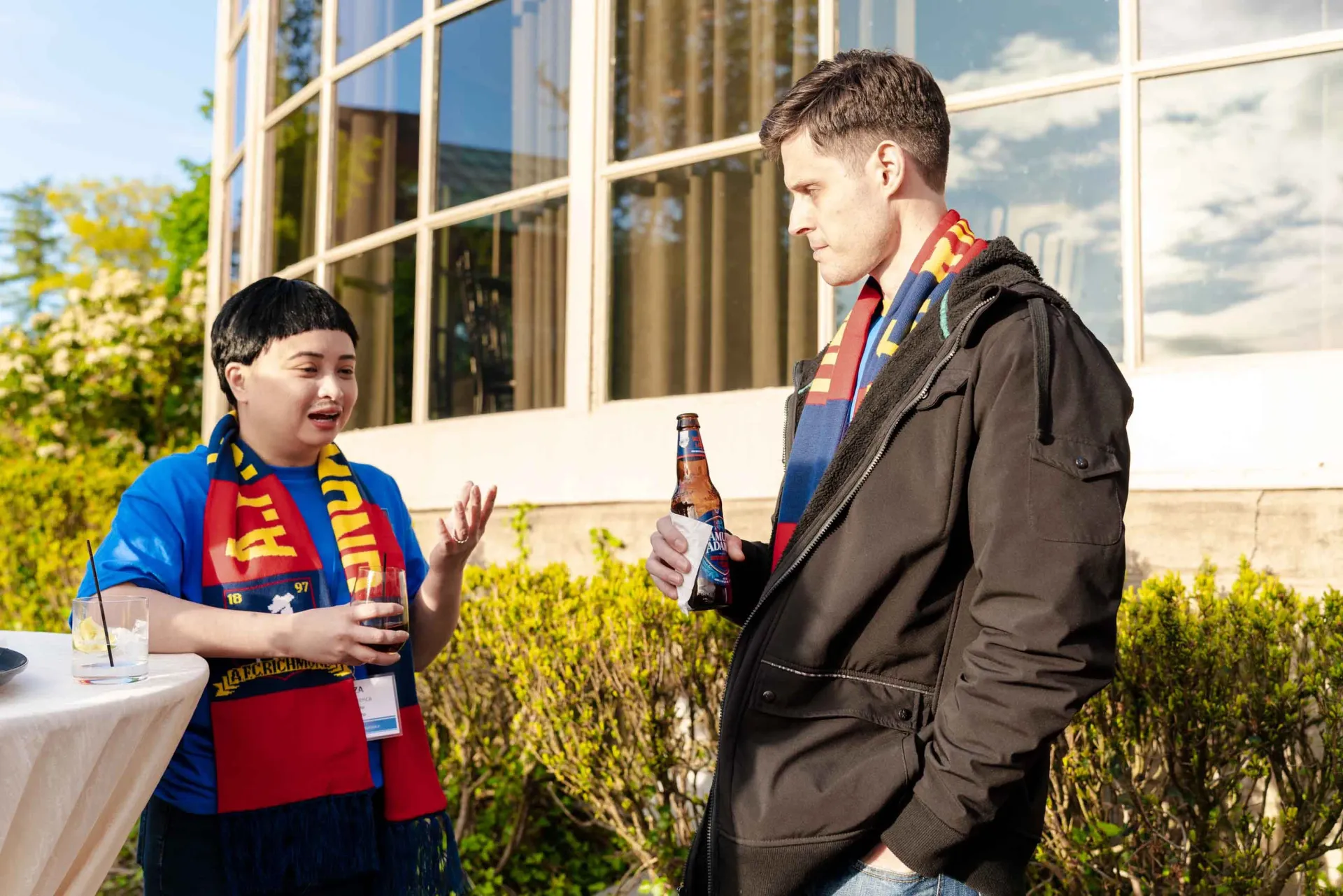 A man and a woman are standing next to each other talking and drinking beer.