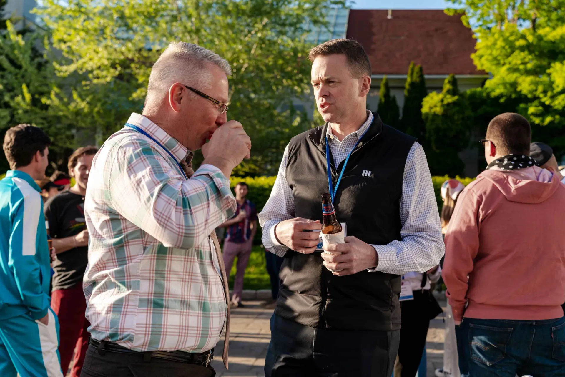 Two men are standing next to each other in a park talking to each other.