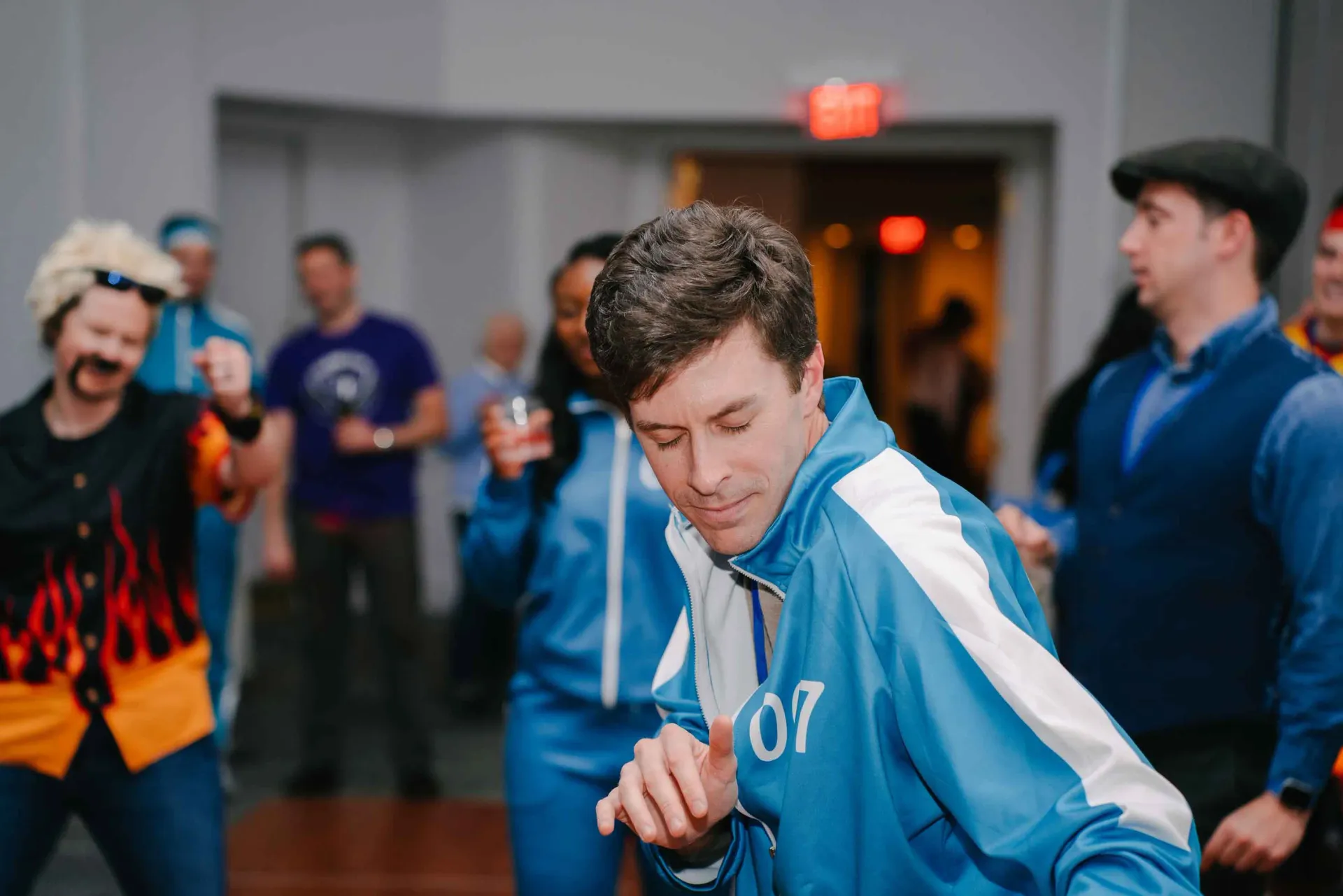 A man in a blue jacket is dancing in a room with other people.