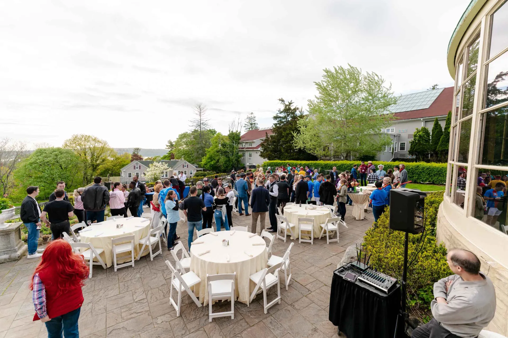 A large group of people are standing around tables and chairs on a patio.