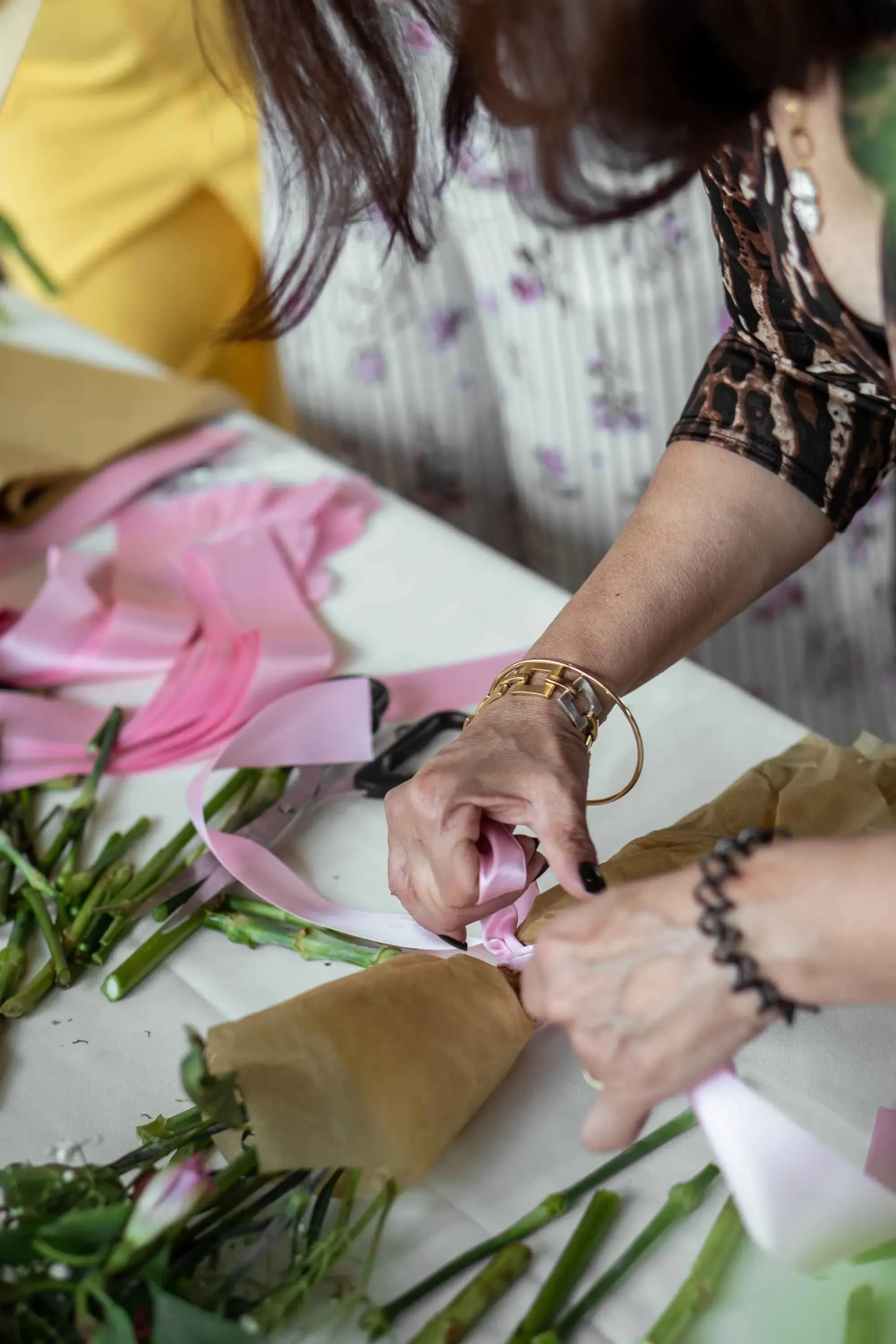 A woman is cutting a pink ribbon on a table with flowers.