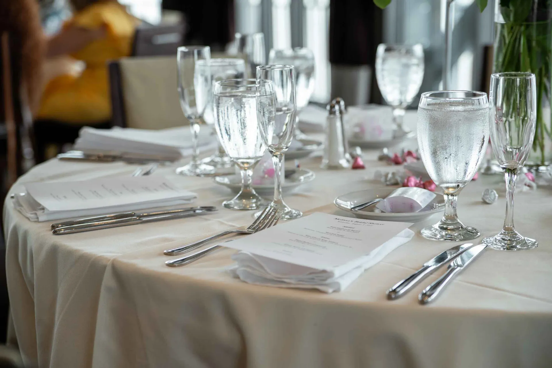 A table set for a wedding reception with glasses of water and silverware.