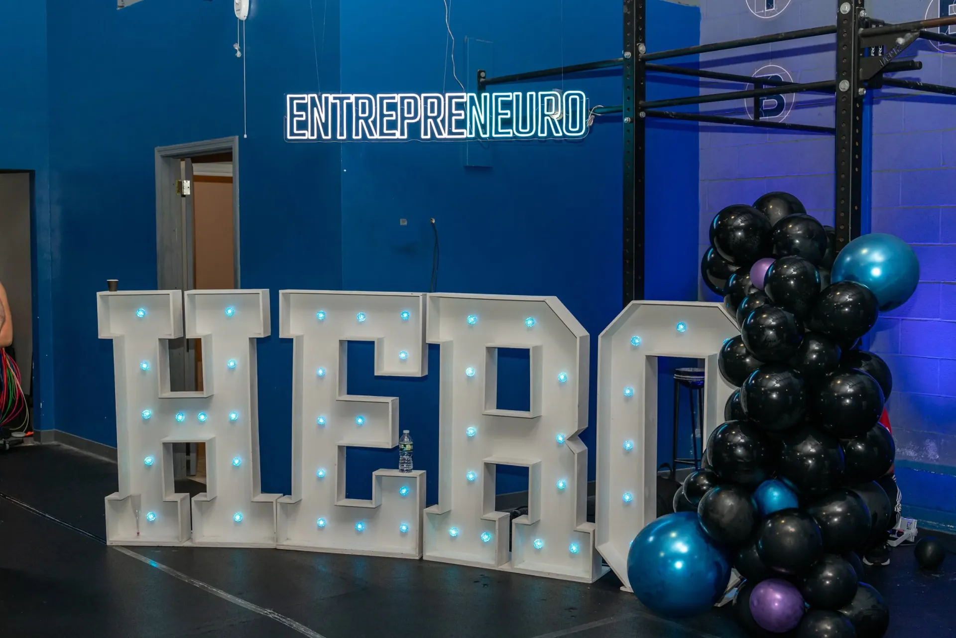 A large sign that says `` hero '' is surrounded by balloons in a gym.