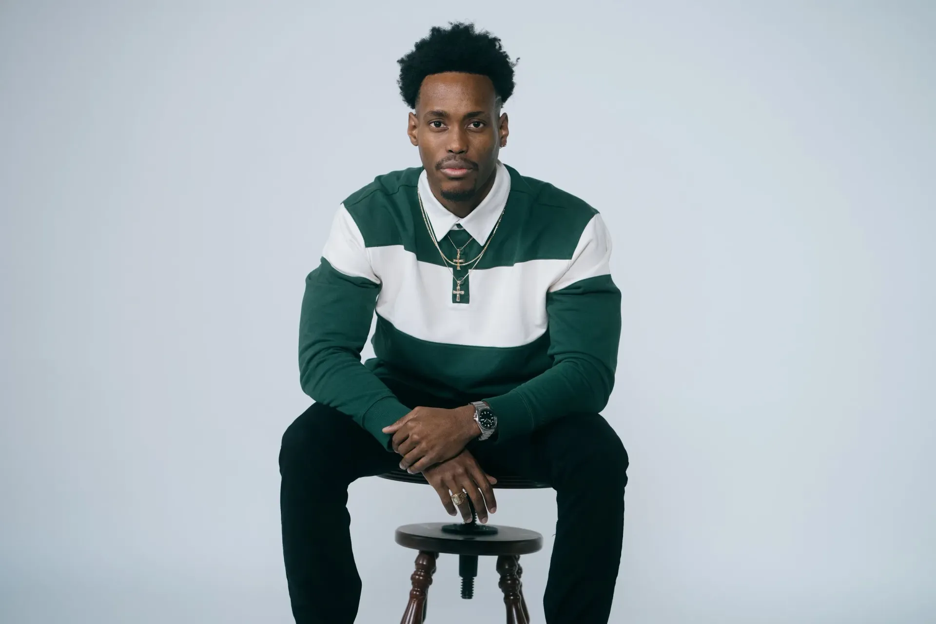 A man in a green and white striped sweater is sitting on a wooden stool.