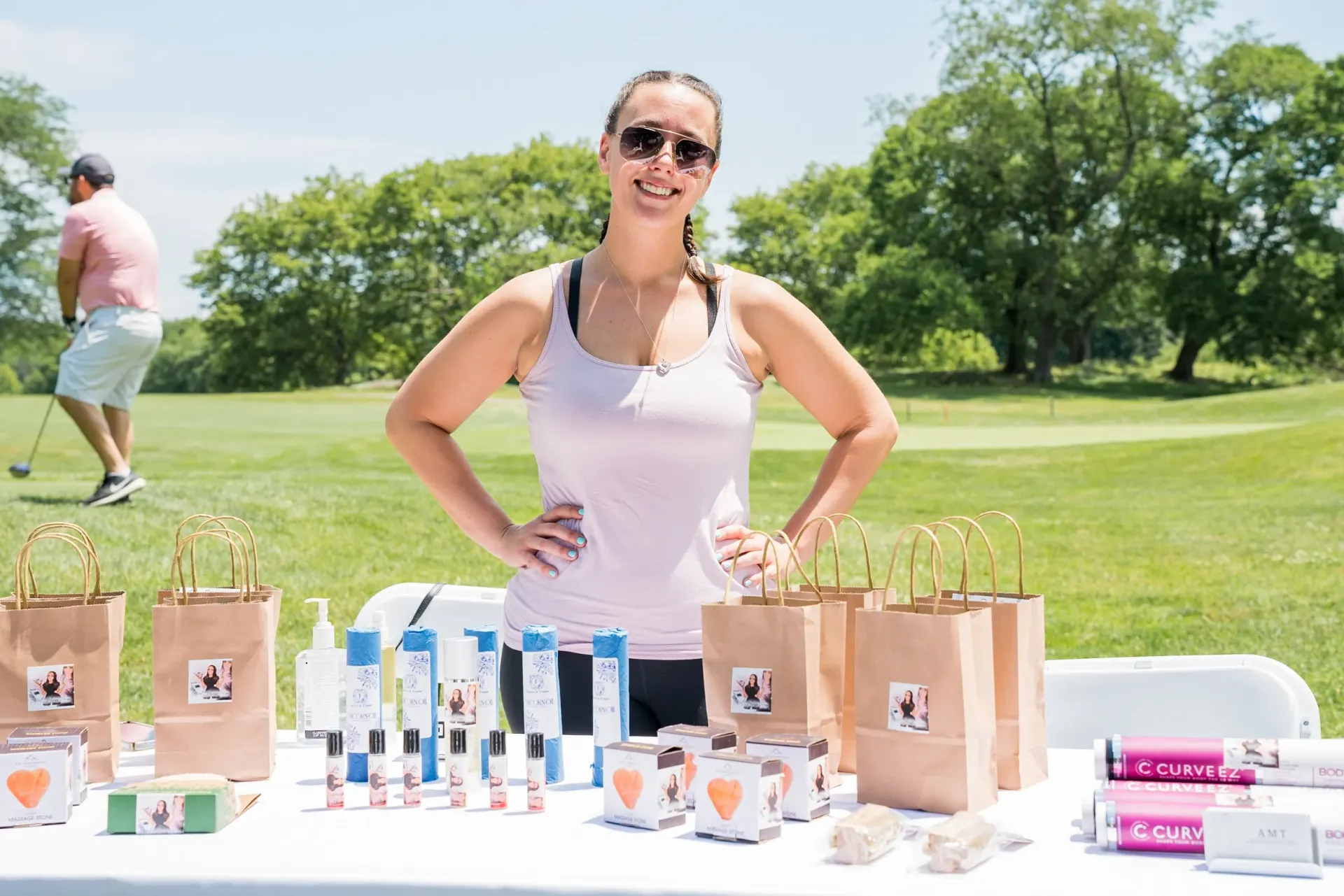 A woman is standing in front of a table with a man playing golf in the background.
