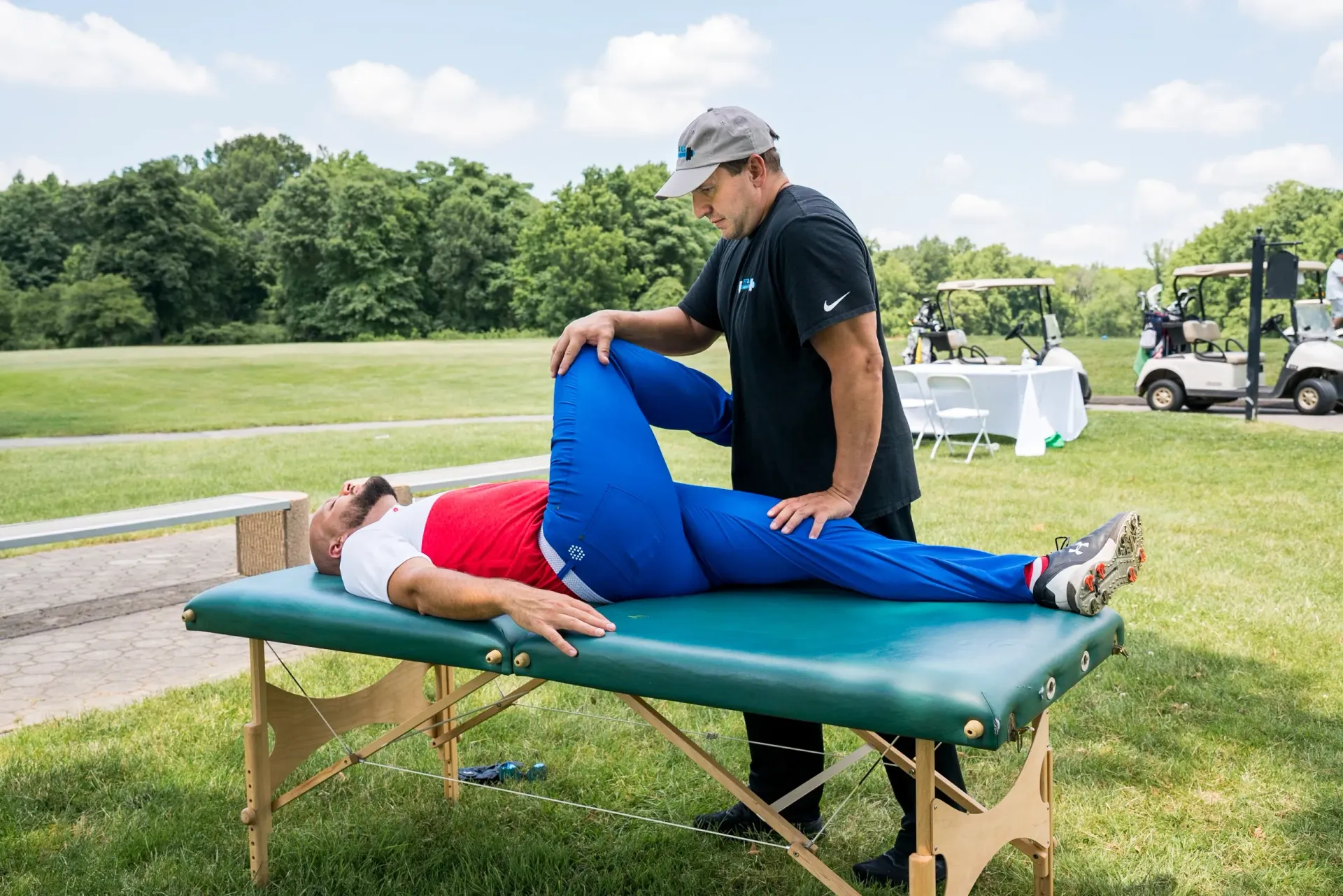 A man is stretching a woman 's leg on a table outside.