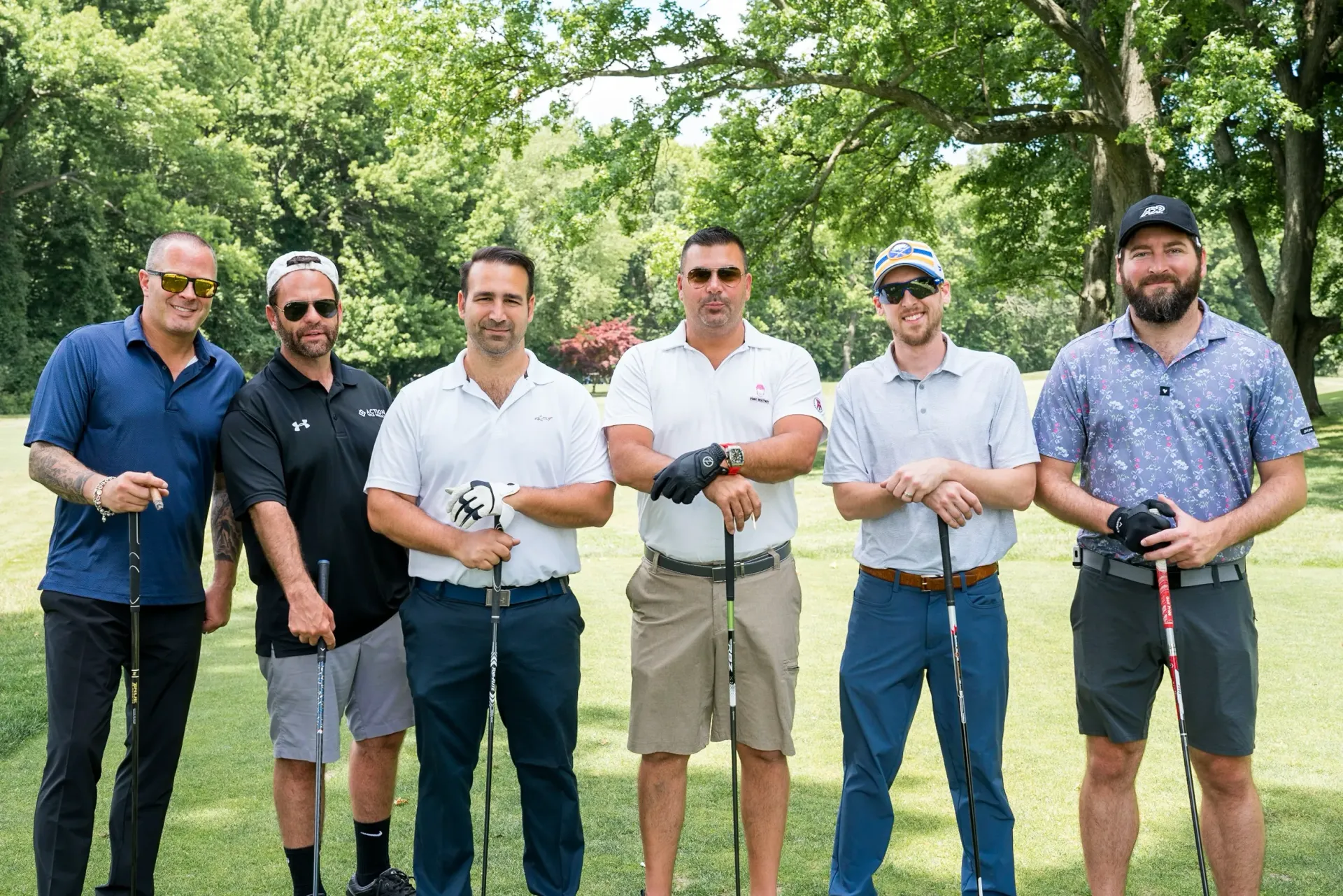 A group of men are standing next to each other on a golf course holding golf clubs.