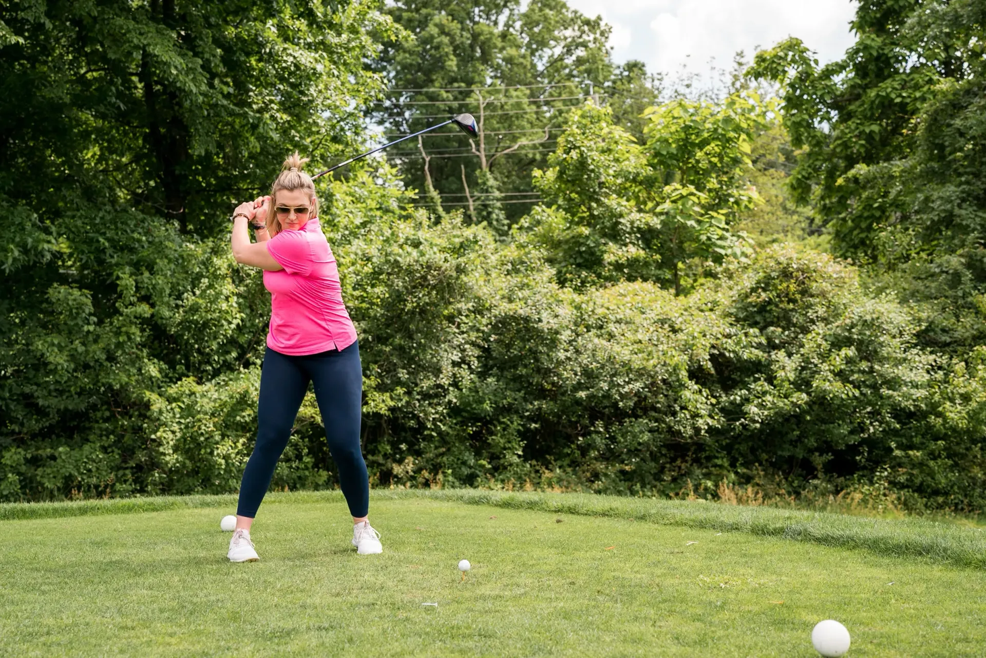 A woman is swinging a golf club at a golf ball on a golf course.
