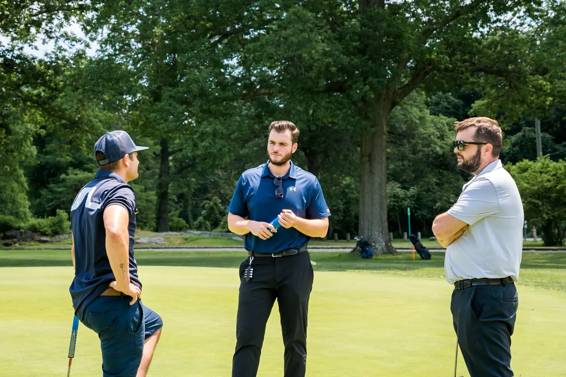 Three men are standing on a golf course talking to each other.