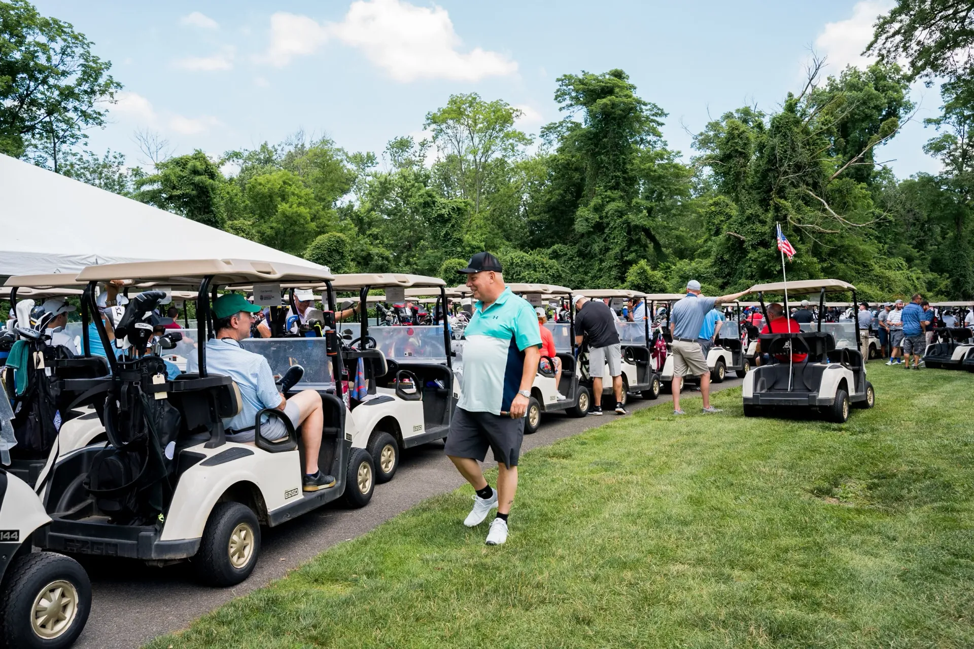 A row of golf carts are parked in a grassy field.