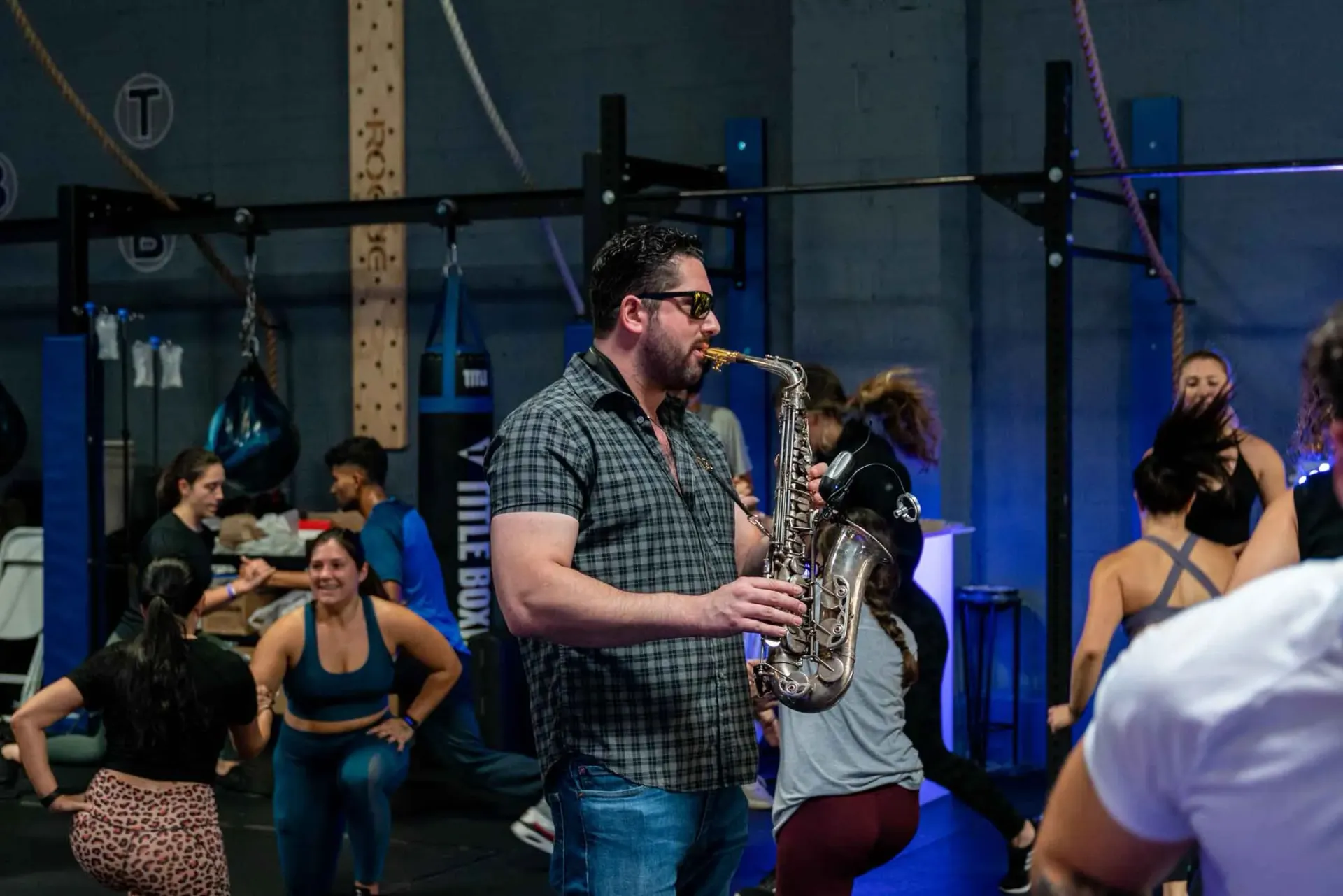 A man is playing a saxophone in front of a group of people in a gym.