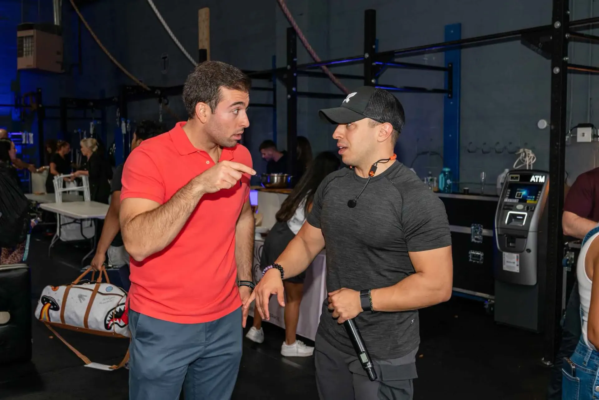 Two men are standing next to each other in a gym talking to each other.