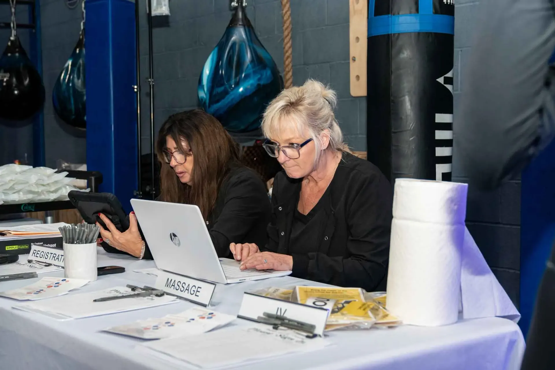 Two women are sitting at a table using laptops.