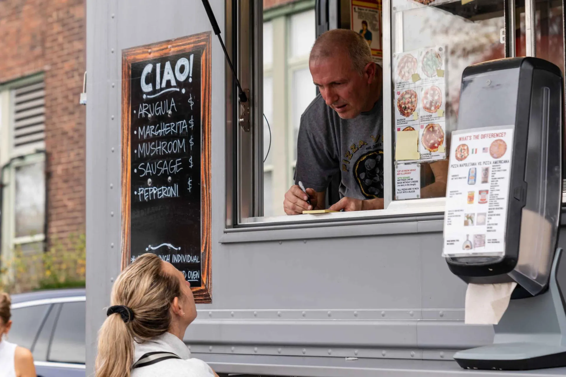 A man is standing in front of a food truck talking to a woman.