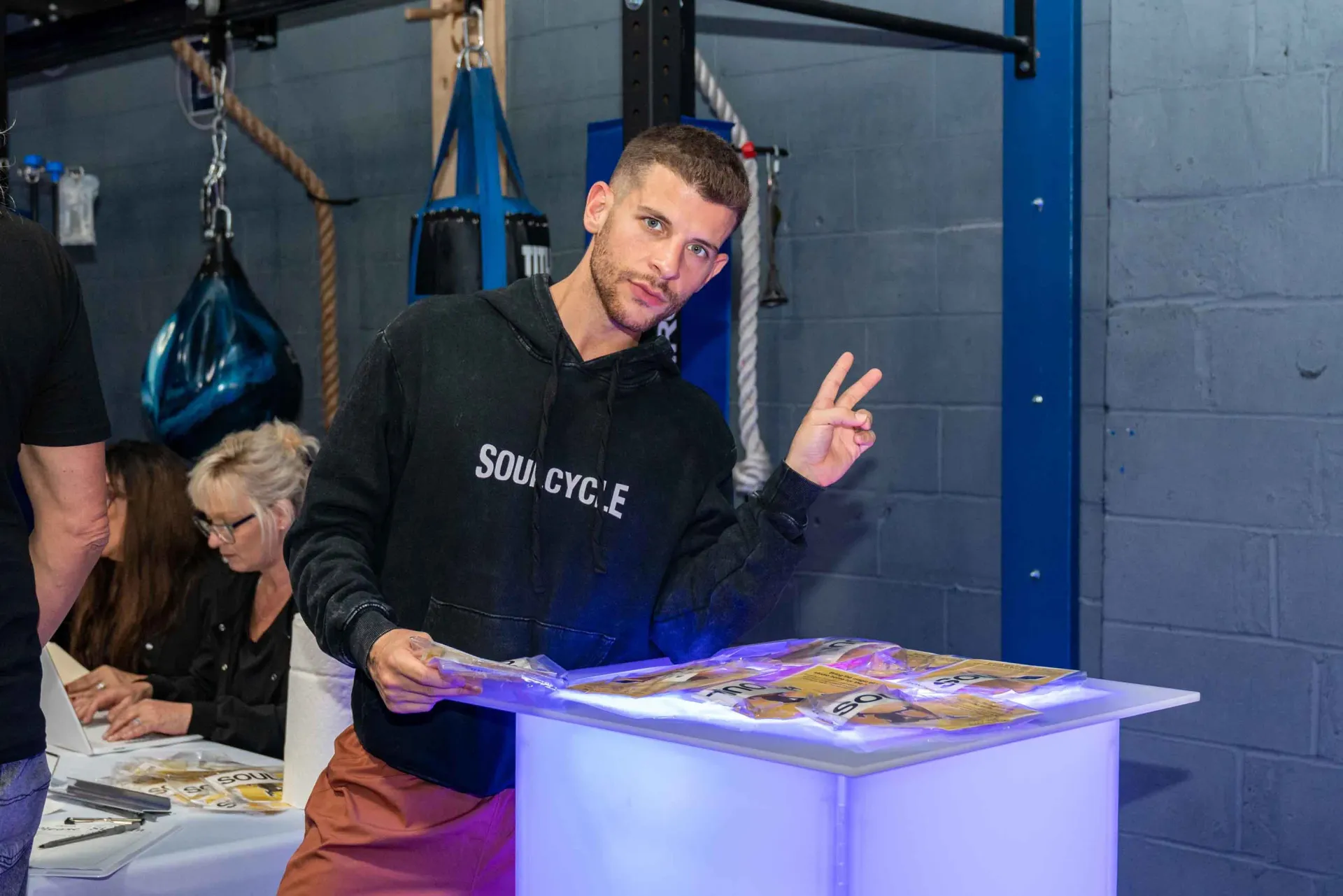 A man in a black hoodie is standing in front of a table.