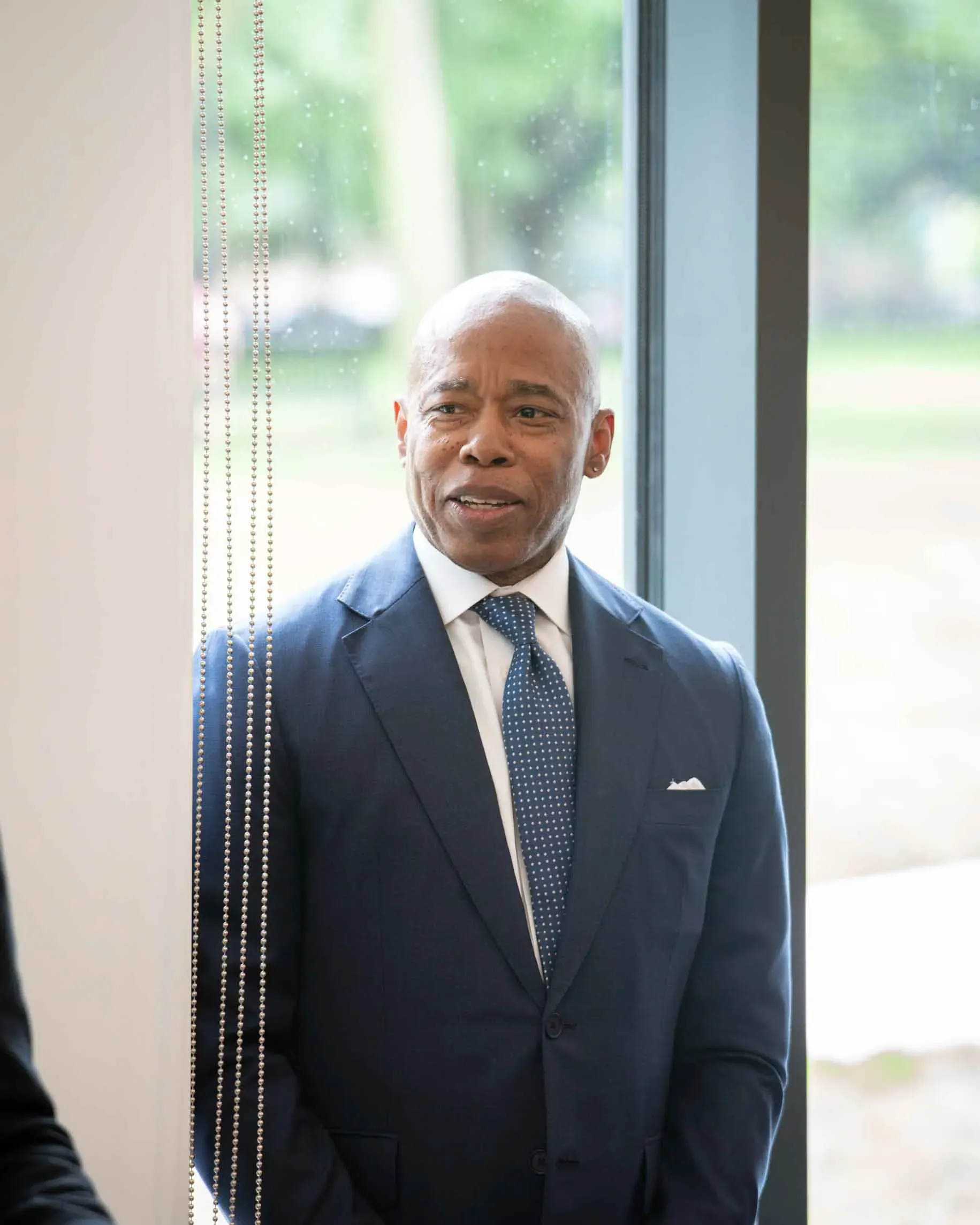 A man in a suit and tie is standing in front of a window.