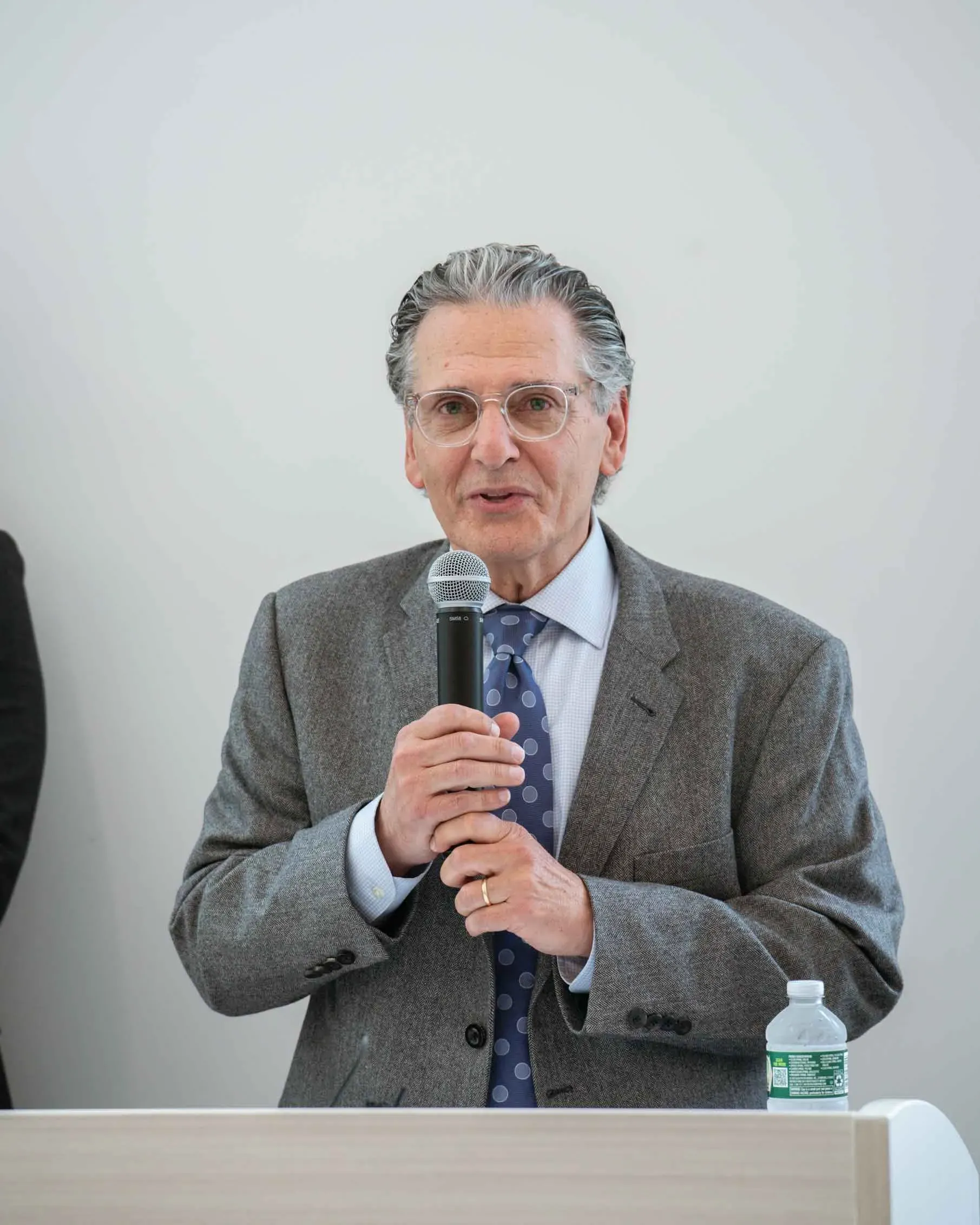 A man in a suit and tie is speaking into a microphone.