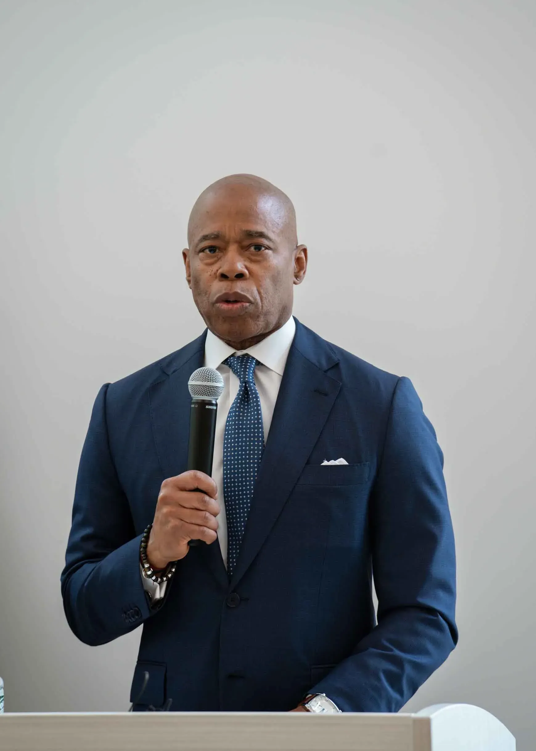 A man in a suit and tie is standing at a podium holding a microphone.