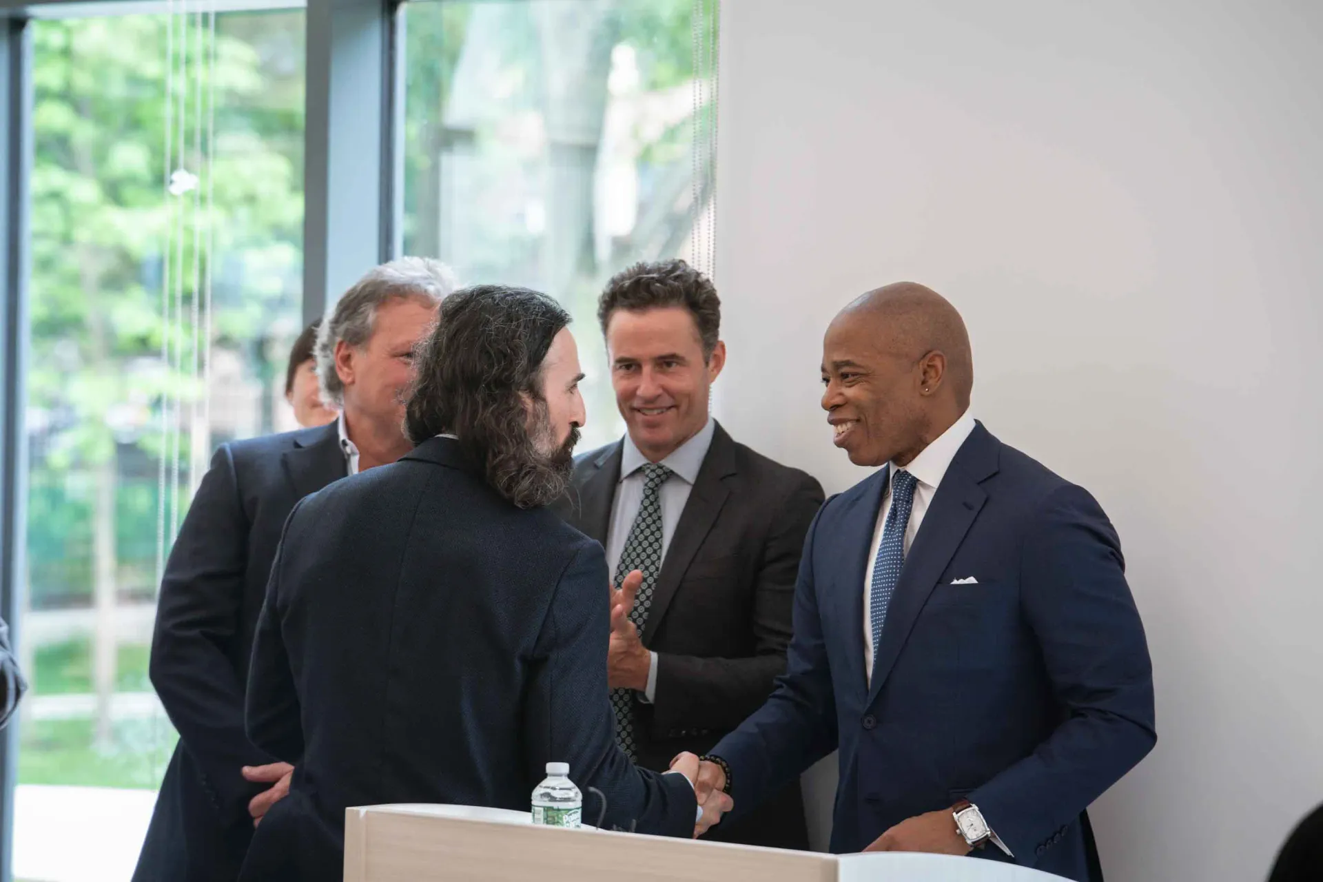 A group of men in suits and ties are shaking hands in a room.