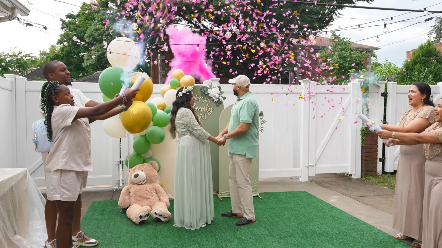 A group of people are standing around a pregnant woman and a teddy bear at a gender reveal party.
