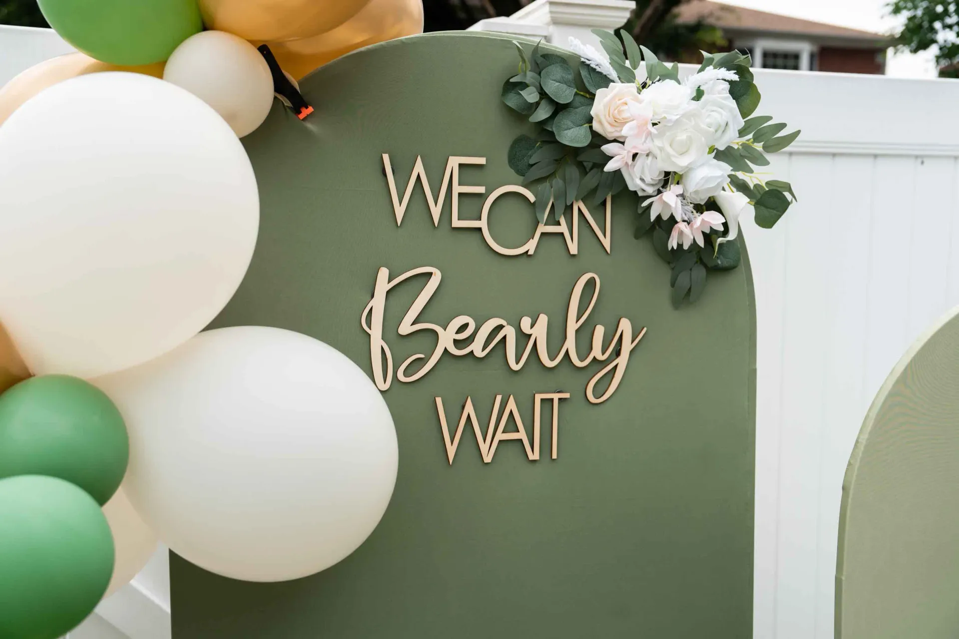 A sign that says `` we can bearly wait '' is surrounded by balloons and flowers.