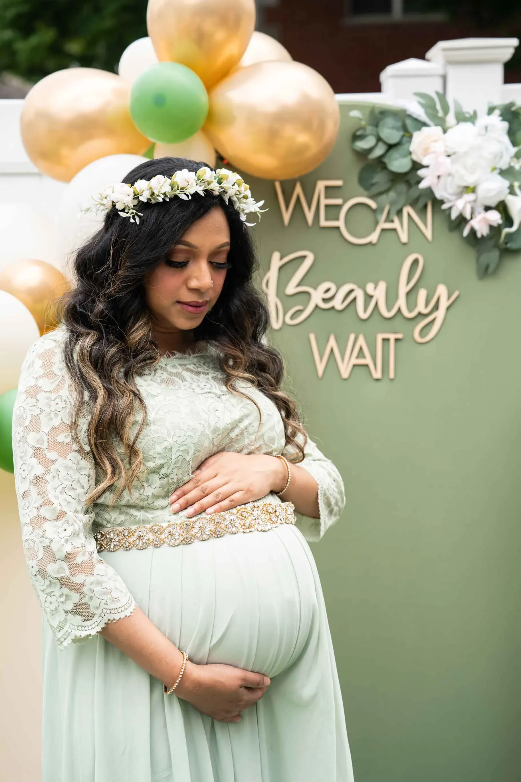 A pregnant woman is standing in front of a wall with balloons and flowers.