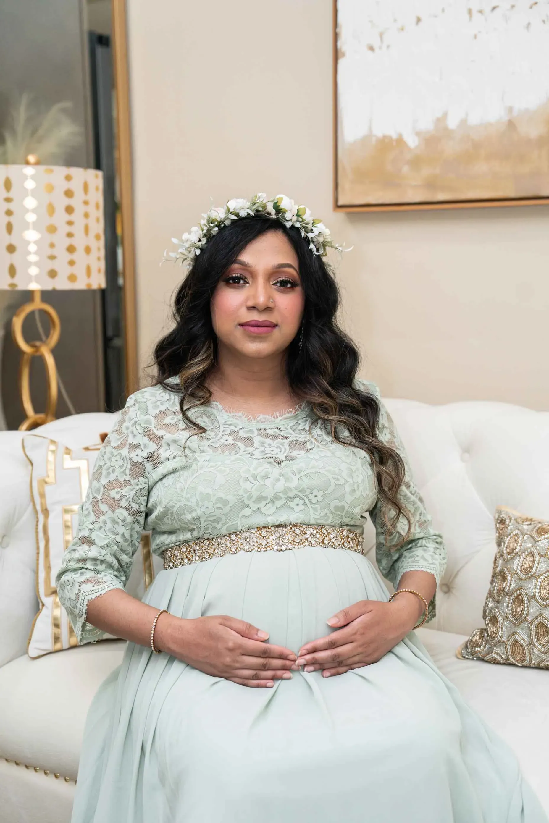A pregnant woman is sitting on a couch wearing a flower crown.