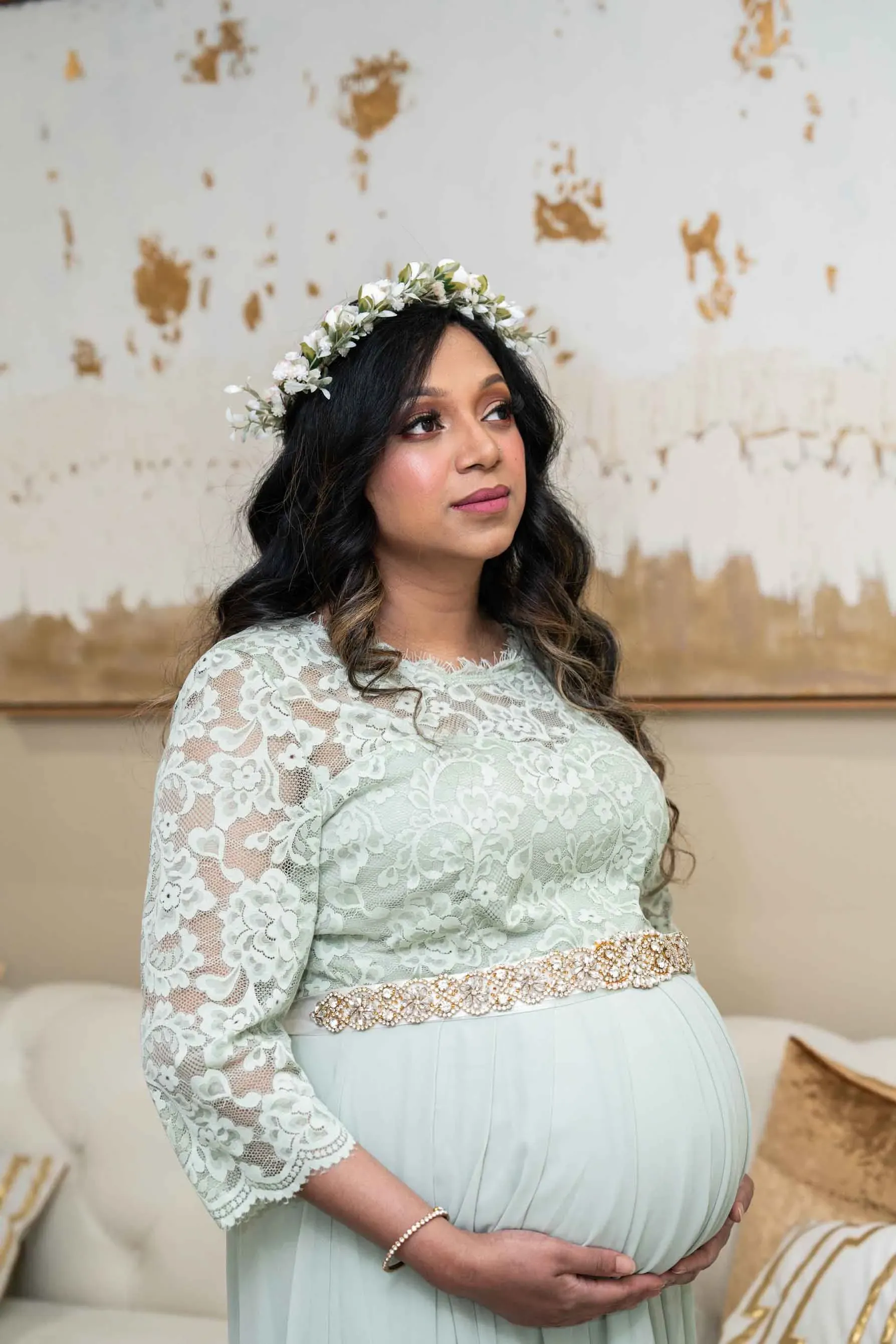 A pregnant woman is wearing a flower crown and holding her belly.