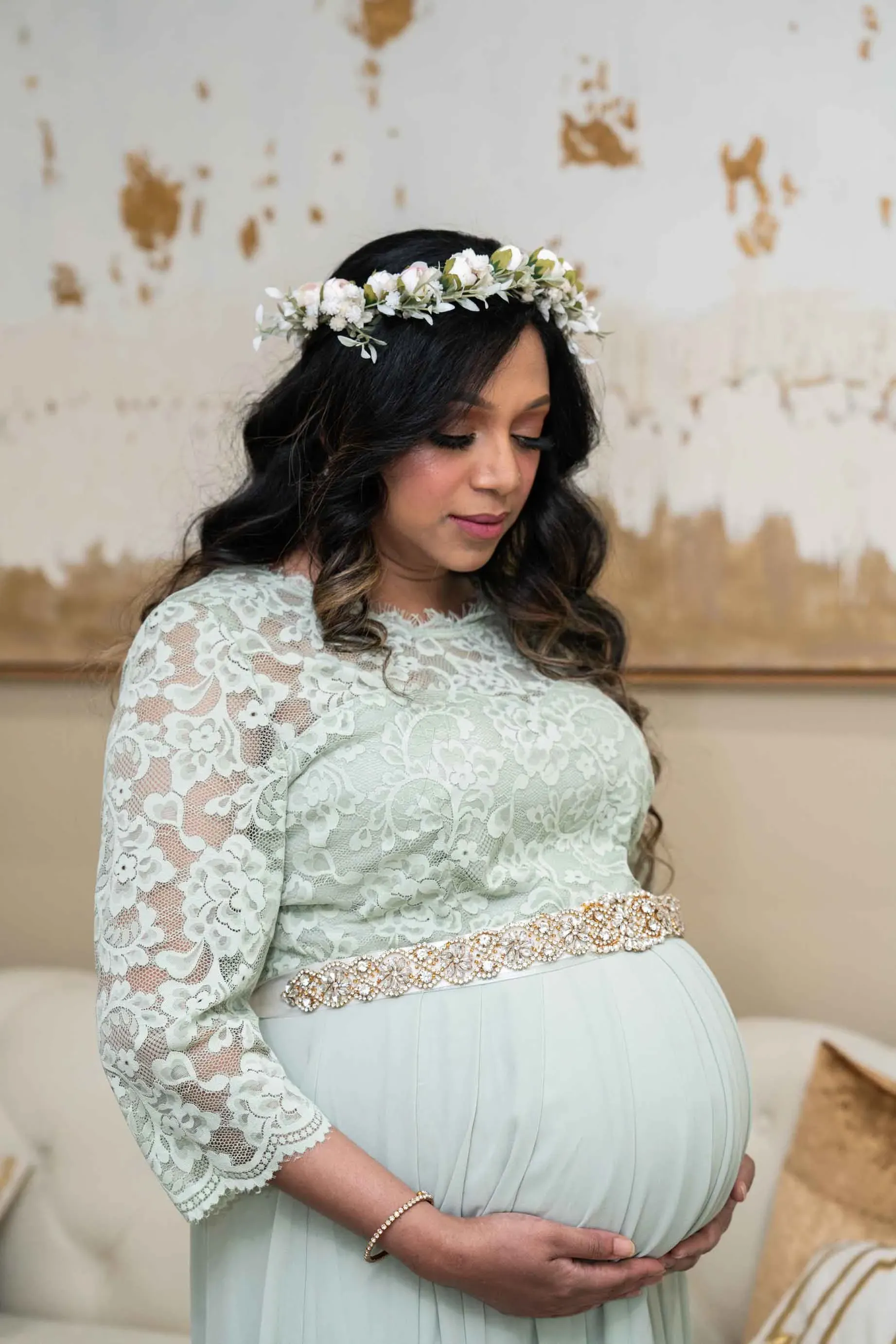 A pregnant woman wearing a flower crown is holding her belly.