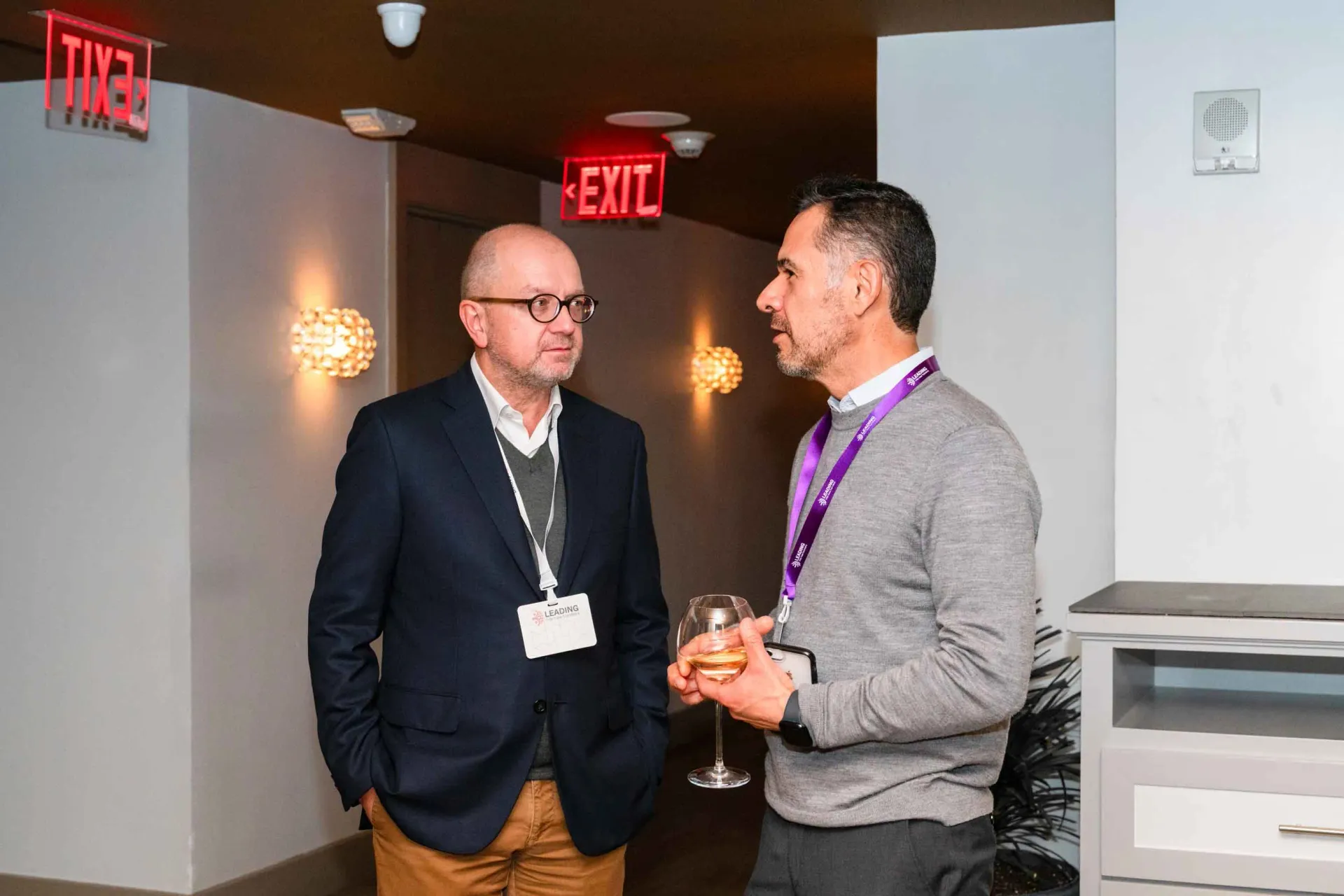 Two men are standing next to each other in front of an exit sign.