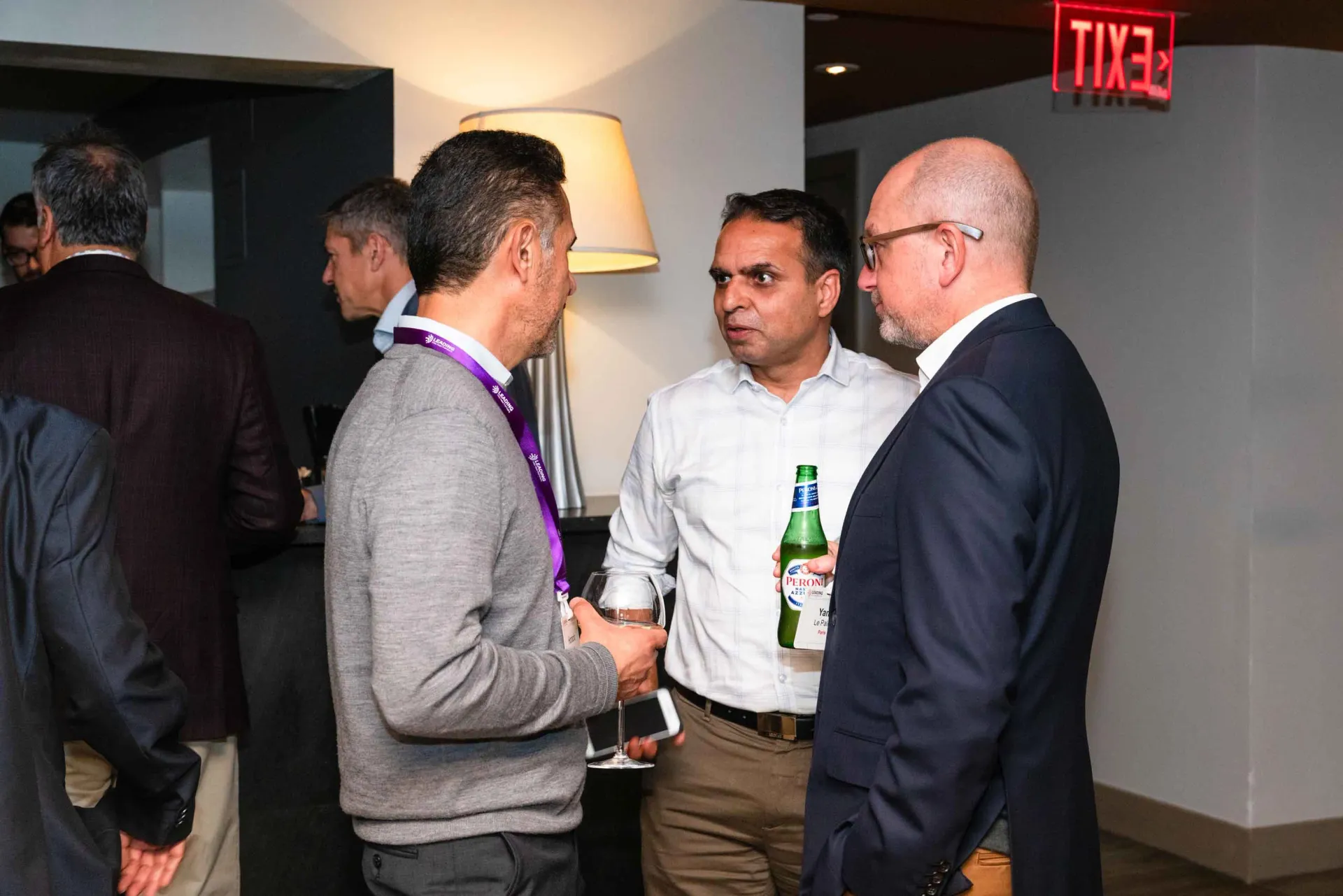 A group of men are standing in a room talking to each other.