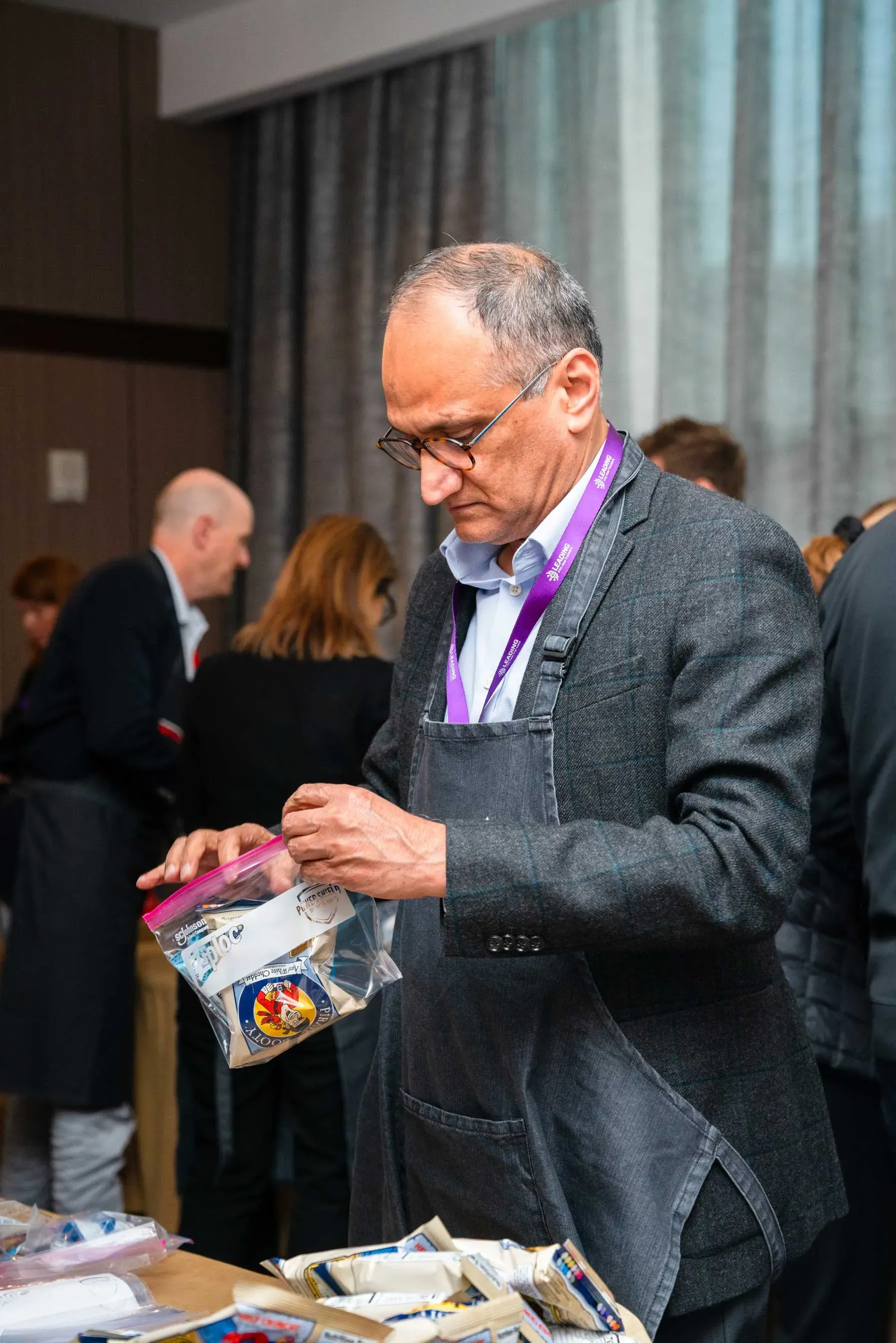 A man in a suit and apron is standing at a table holding a bag of food.